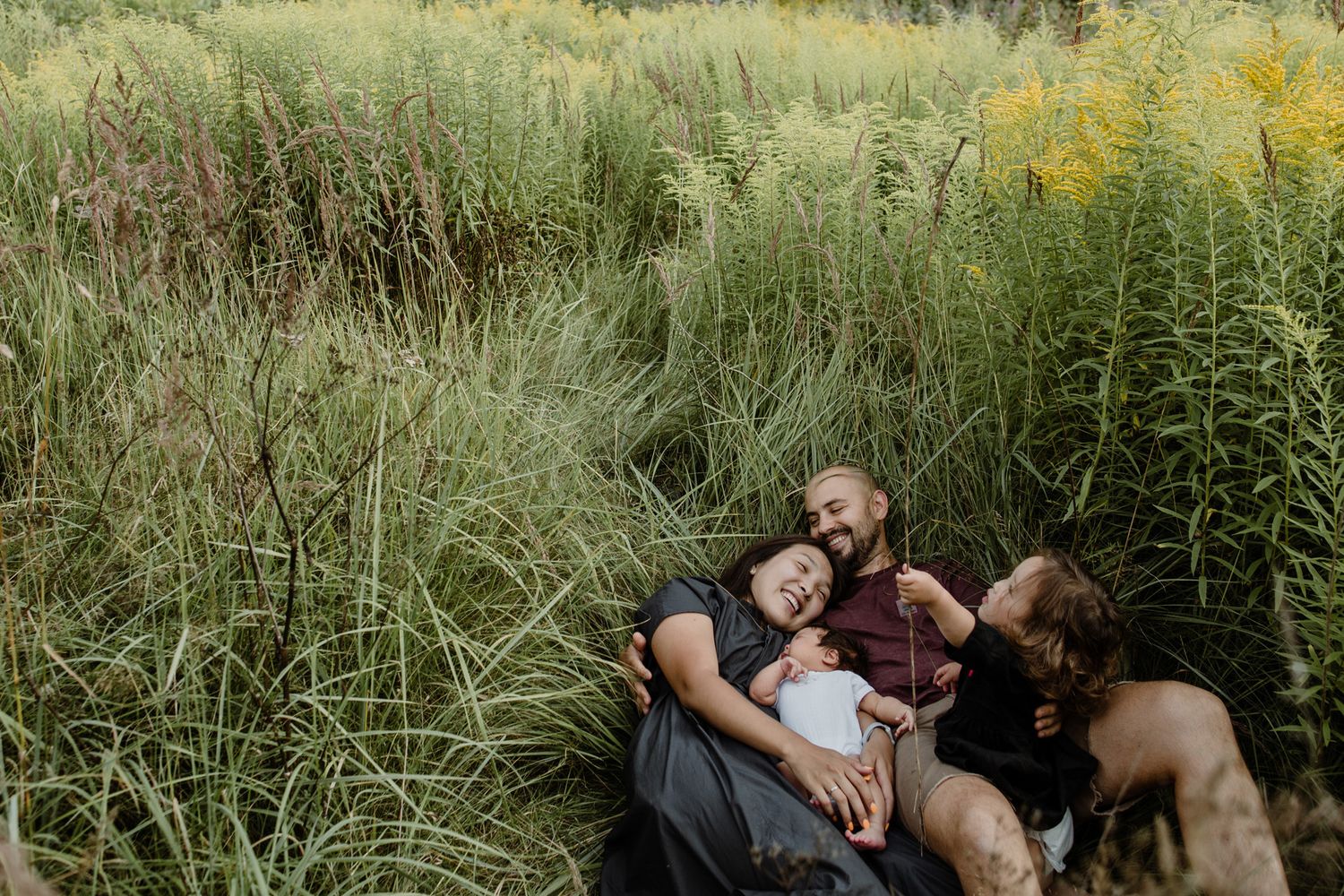 A couple relaxes together in a serene meadow with tall grass and wildflowers on a sunny afternoon.