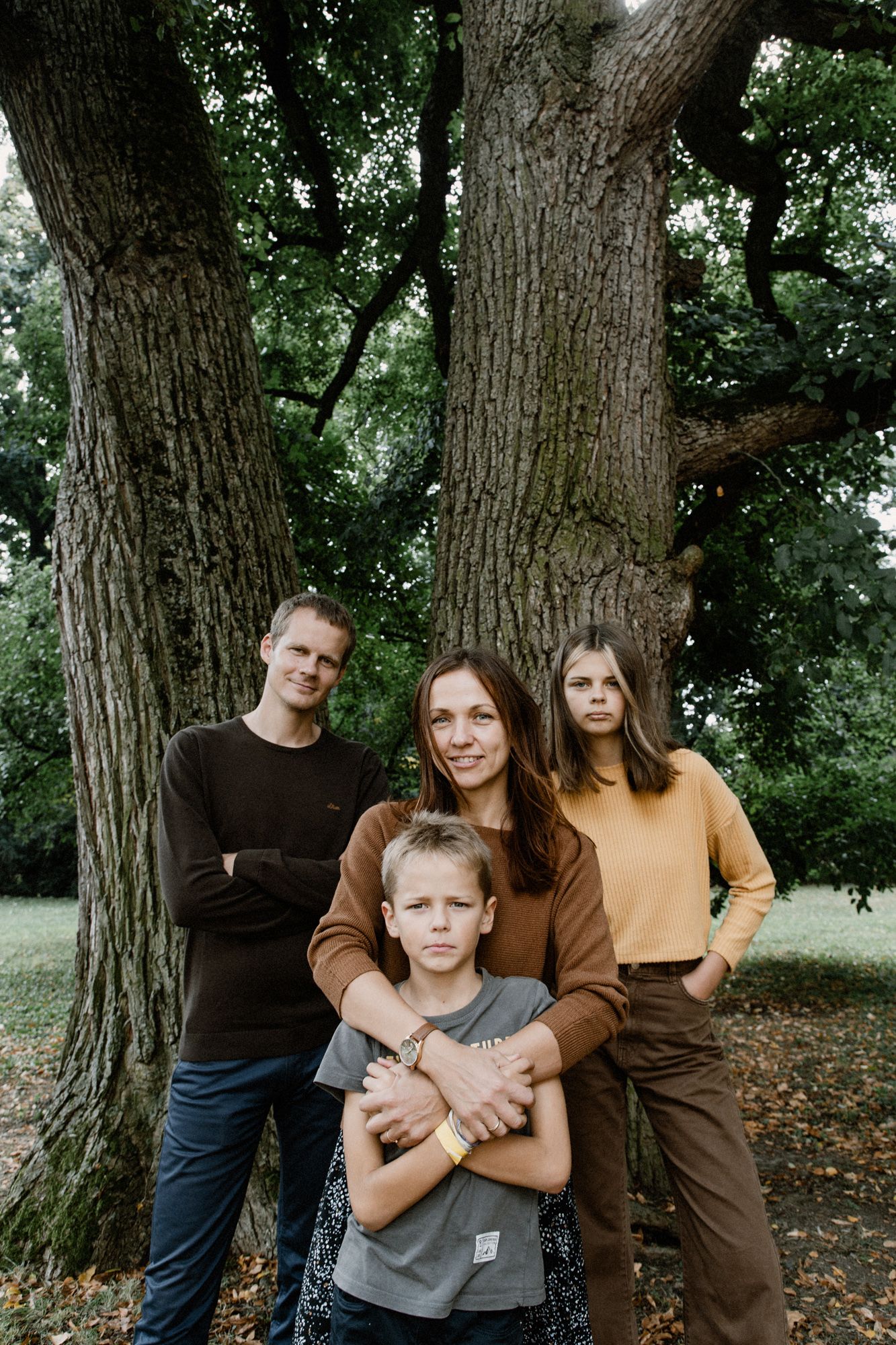 A family poses together against large tree trunks in a wooded outdoor setting.