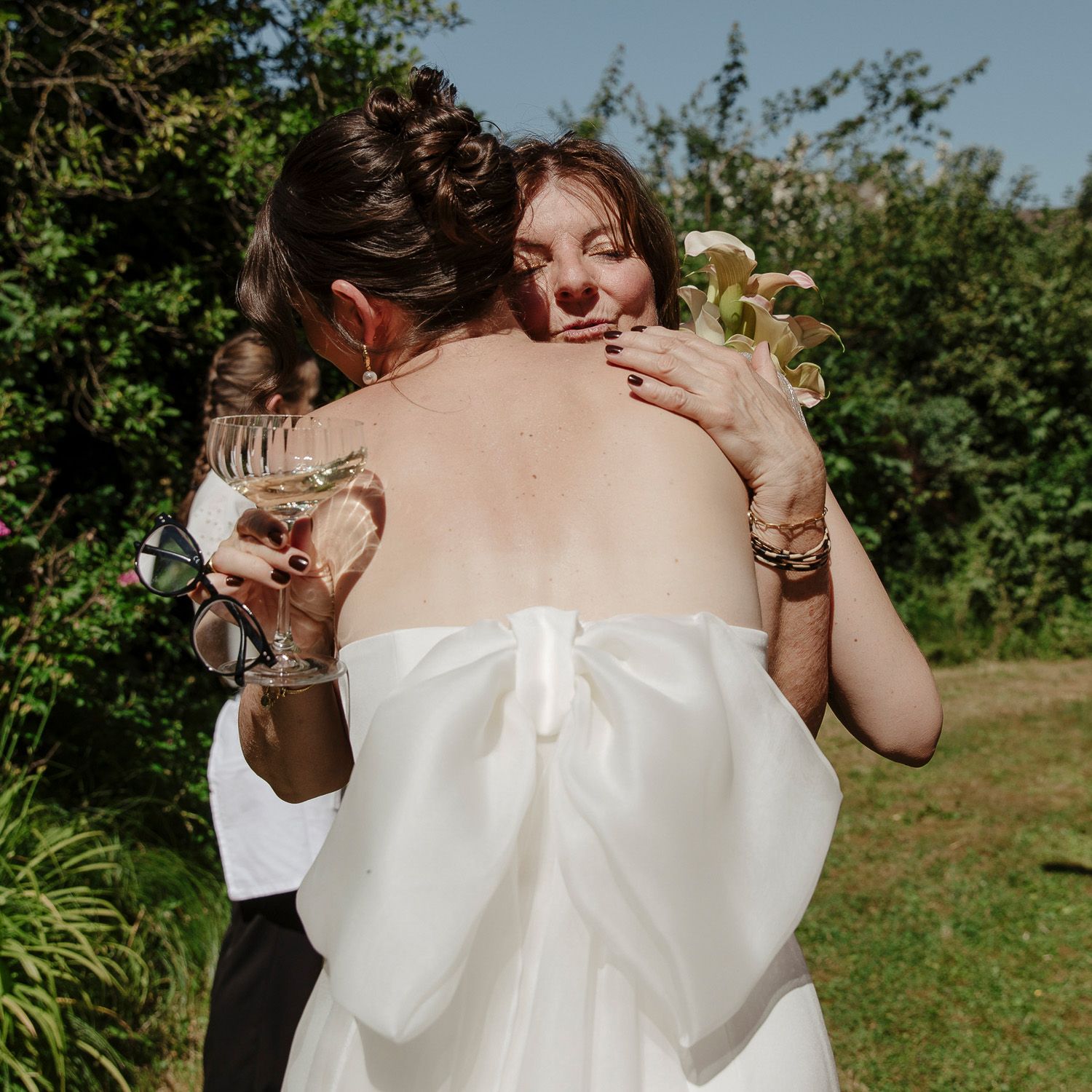 A couple in white clothing dances together in a sunny outdoor garden setting.