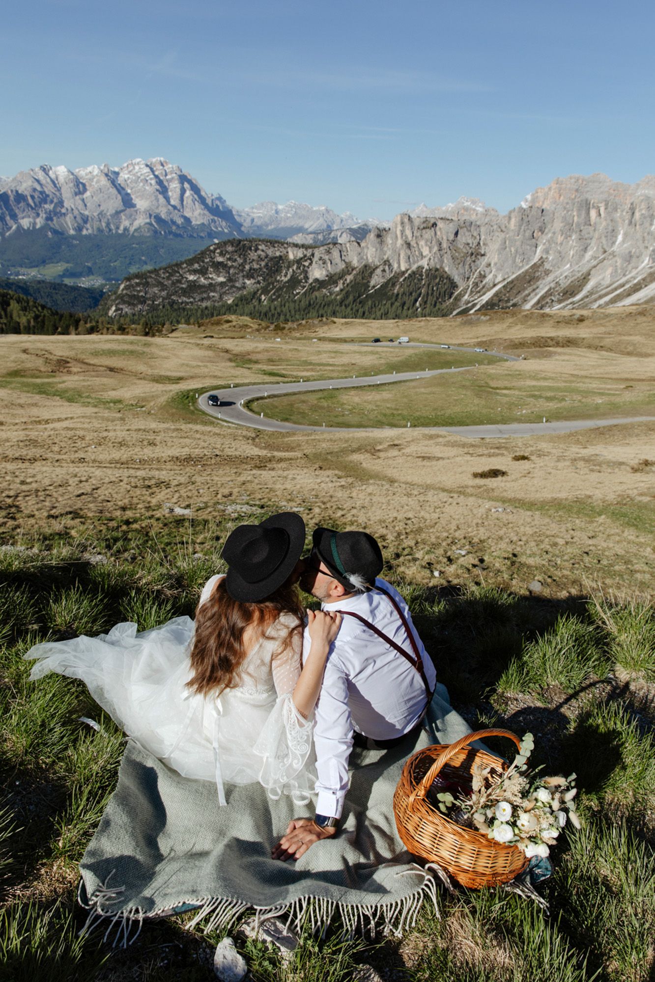 A couple shares a romantic picnic with a woven basket on a blanket overlooking scenic Dolomites mountains in Italy.