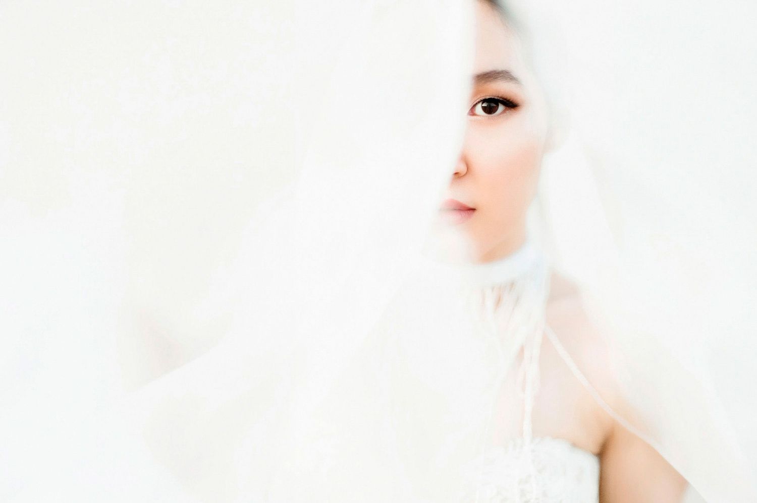 Two people wearing white outfits and headpieces pose in an ethereal setting with soft lighting and dreamy atmosphere.