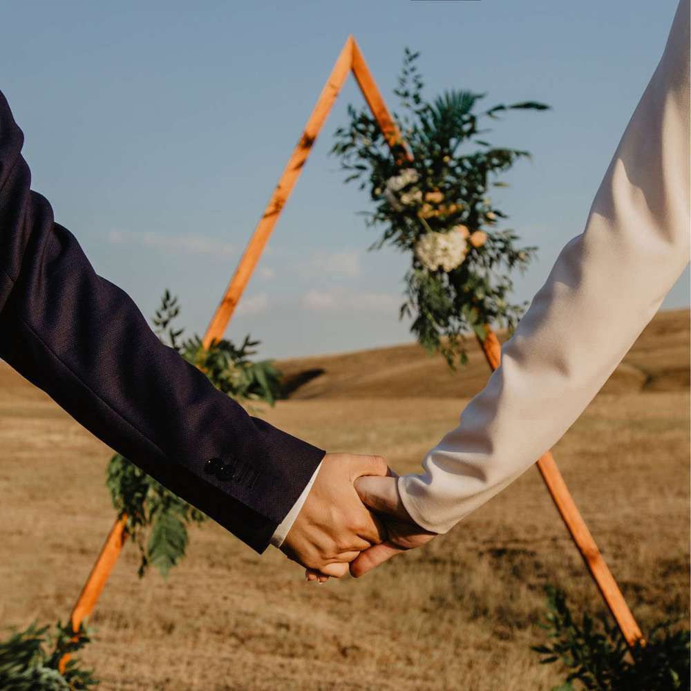 Two hands hold orange paper straws against a blurred outdoor background with dry grass and blue sky.
