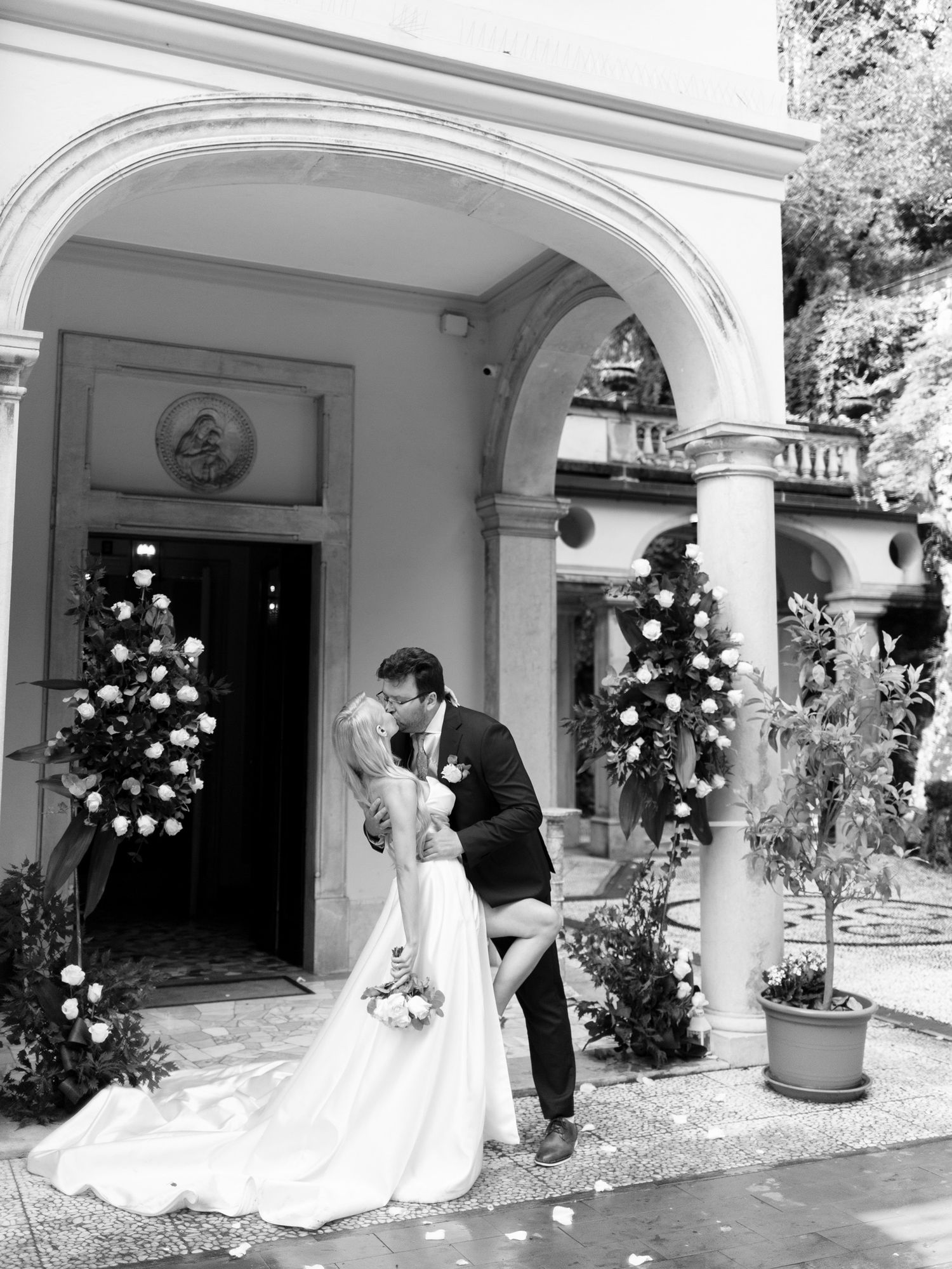 A black and white wedding photo sequence showing a couple dancing and embracing under elegant arched columns.