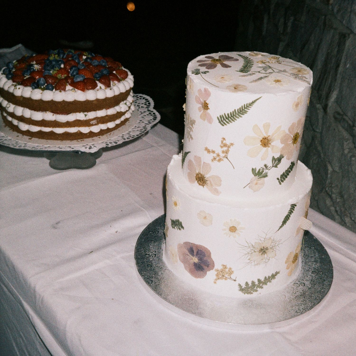 A collection of elegant wedding cakes displayed side by side with delicate floral decorations and rustic fern details.