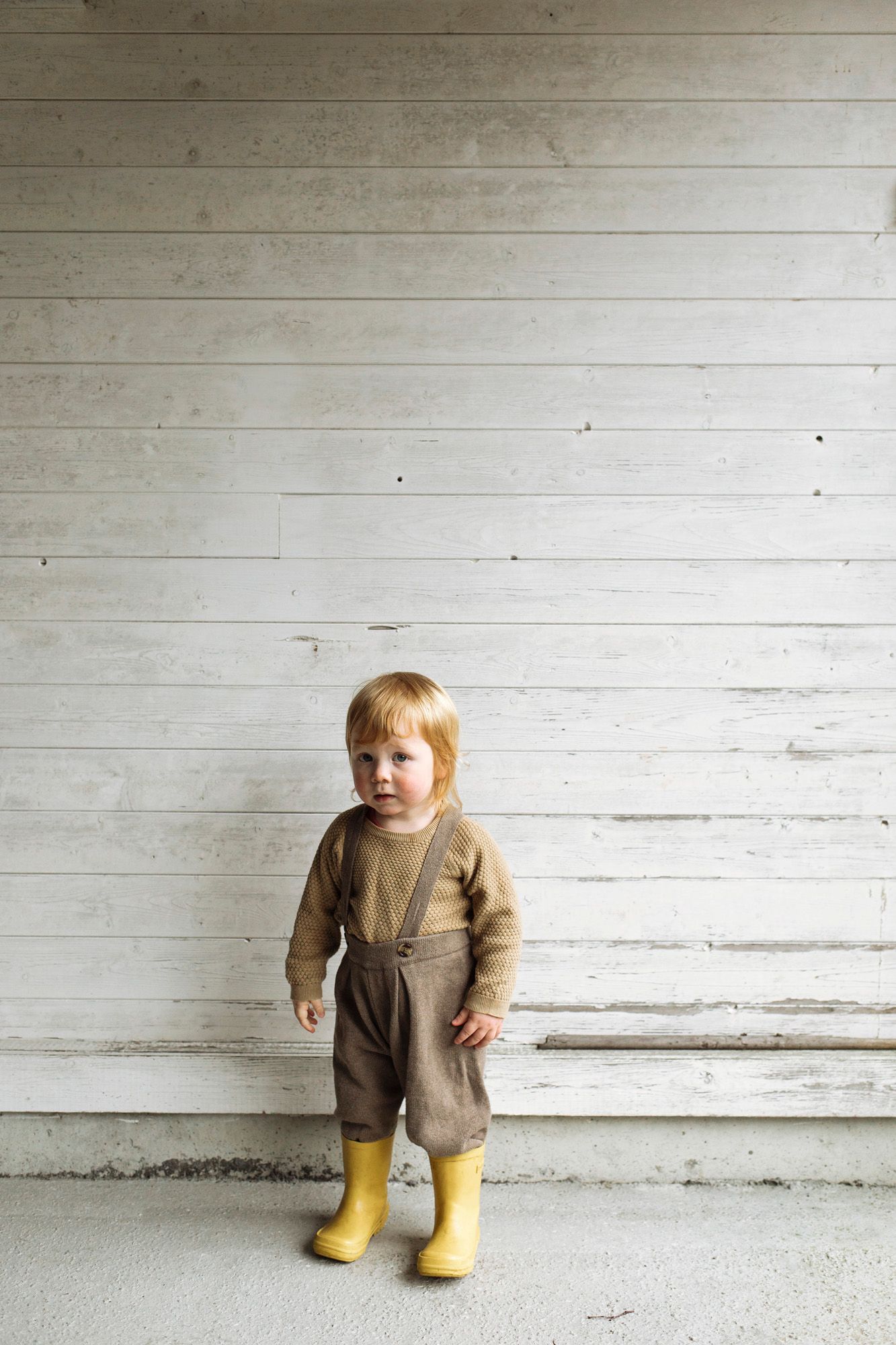 Vintage-inspired brown outfit with yellow rain boots against white wooden wall background.