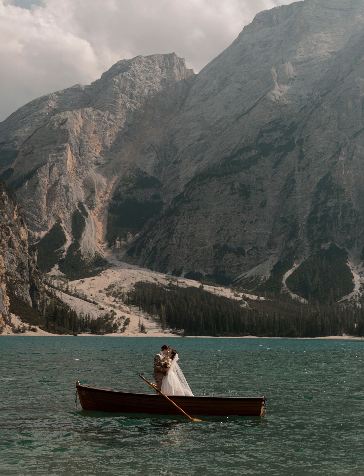 Bride and groom share a romantic moment in a wooden canoe on a turquoise alpine lake with dramatic mountain backdrop.