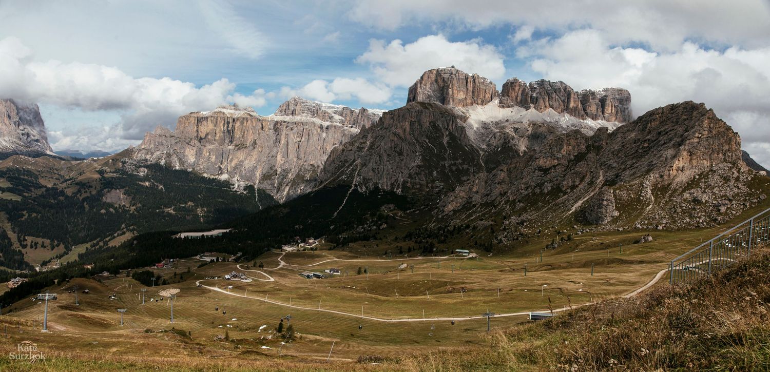 Dramatic mountain landscape panorama with rugged peaks and green valleys in the Dolomites under cloudy skies.