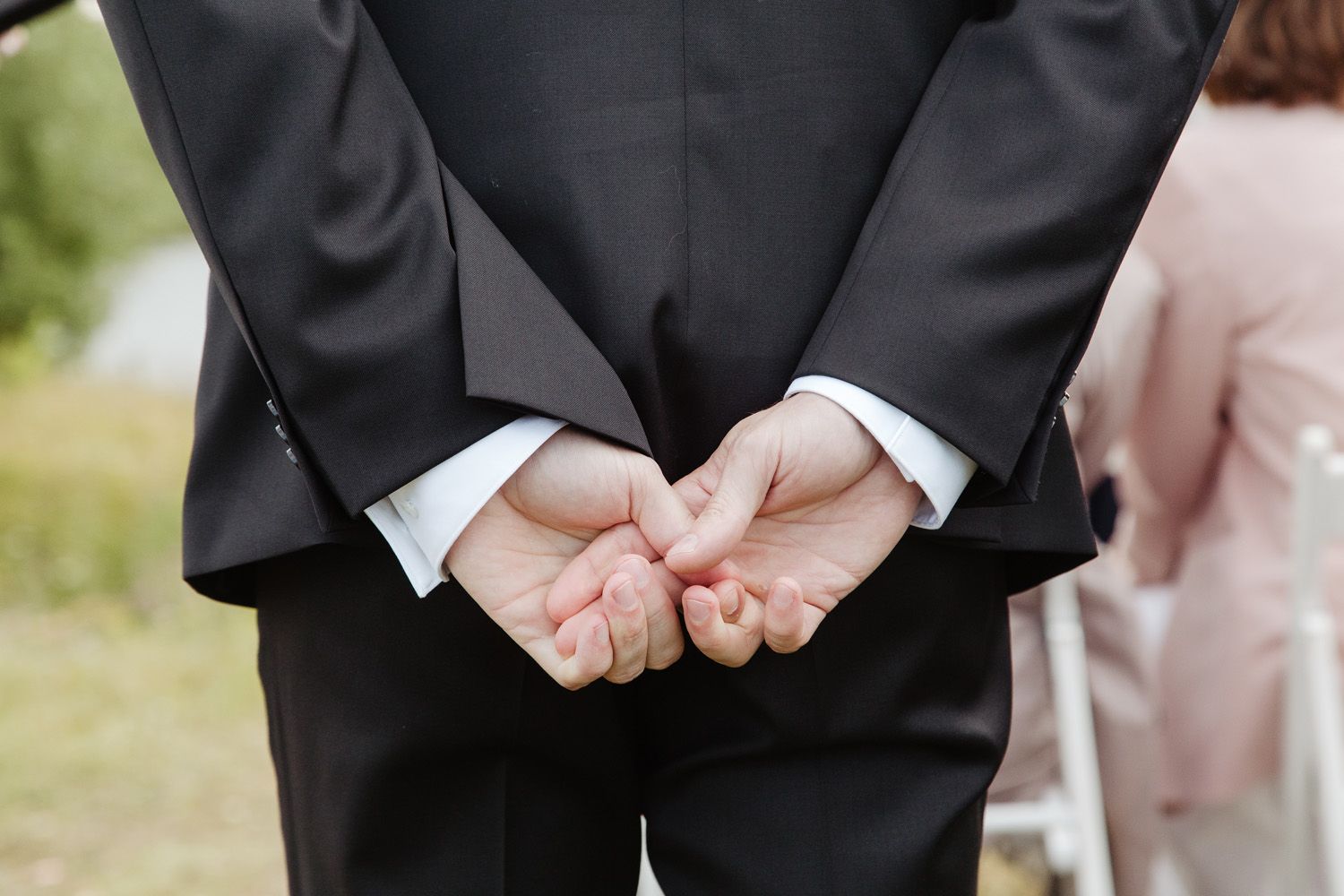 Close-up of hands clasped behind back in formal black suit jacket.