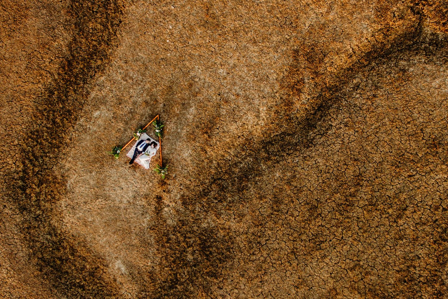 Aerial view of a single car driving on a winding dirt road through arid desert terrain.