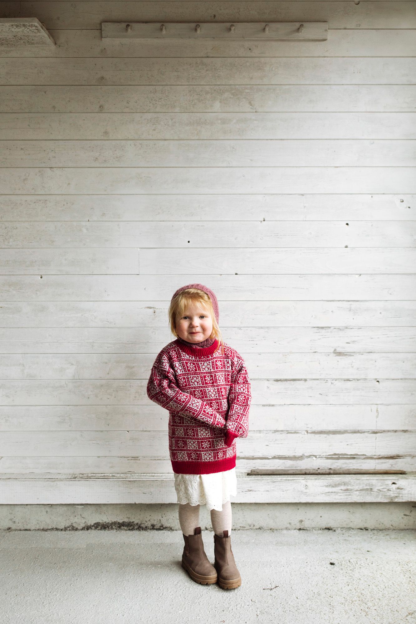 Festive red patterned winter sweater paired with white tights and brown boots in minimalist setting.