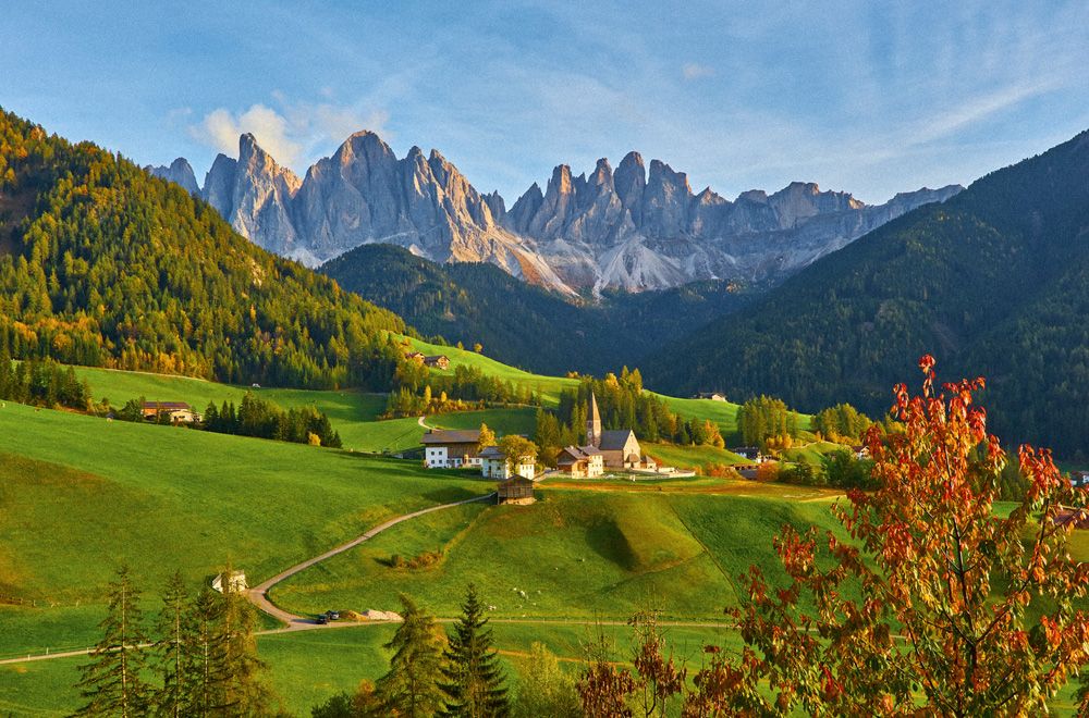 Autumn landscape panorama of mountain village with church nestled in green valley below rugged peaks.
