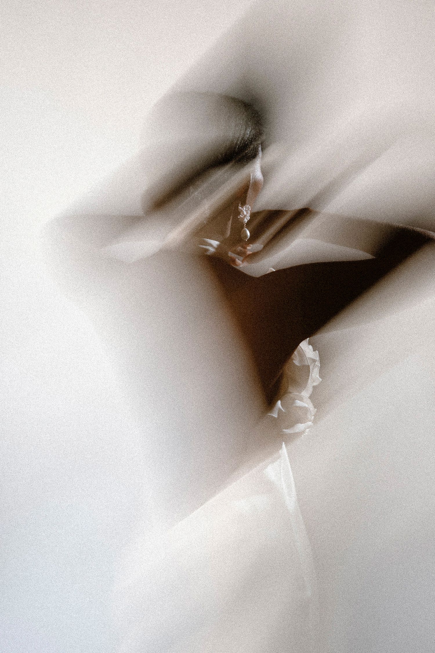 Abstract artistic photograph with soft blurred white shapes creating an ethereal movement effect against a dark background.