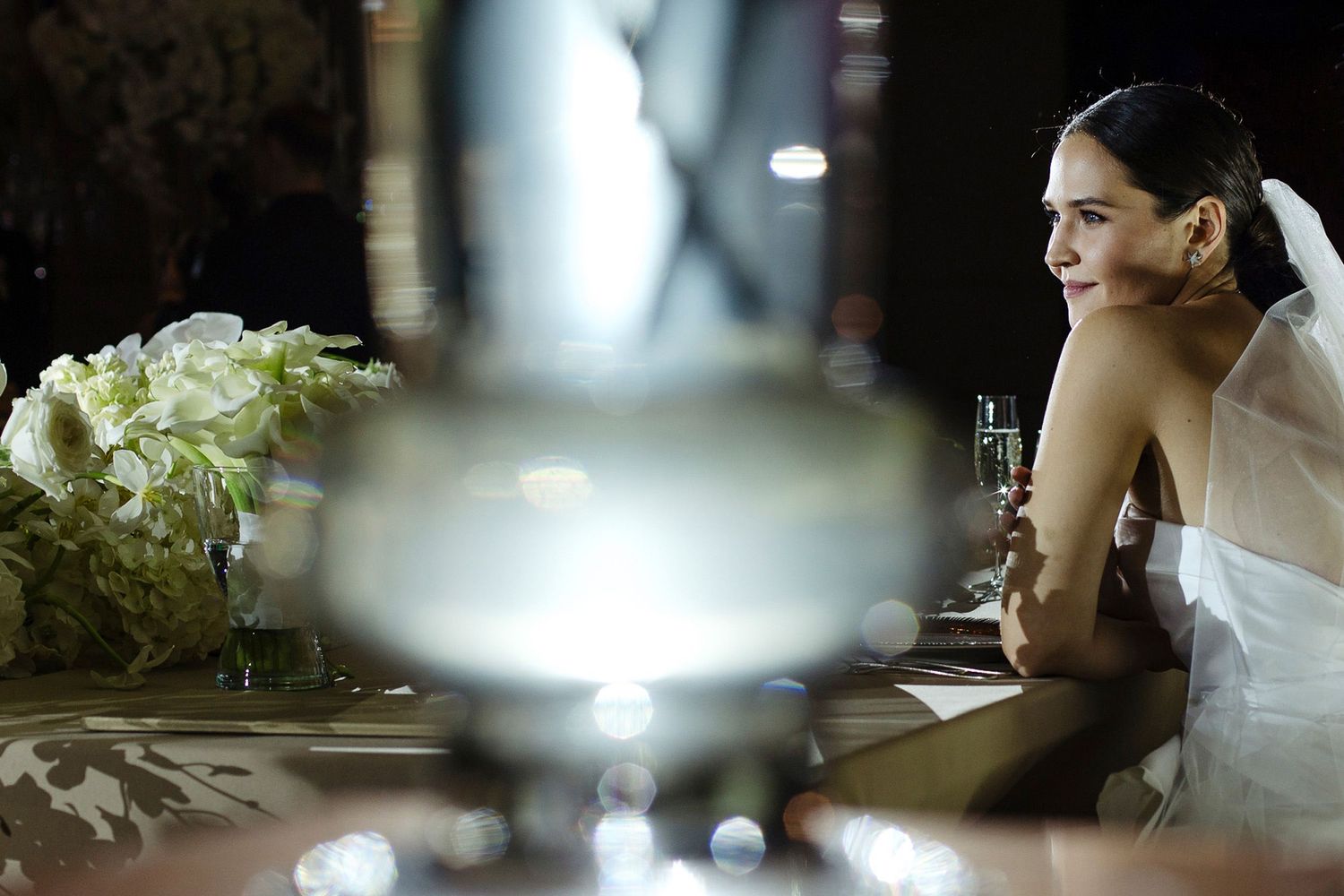 Bride and groom share intimate moments during their wedding reception in dim lighting with white floral decor.
