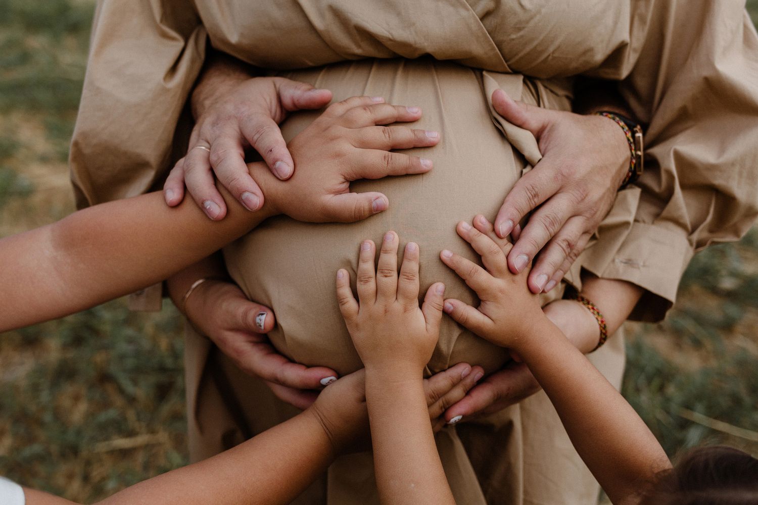 Close-up view of multiple hands touching and overlapping in a warm outdoor setting with natural lighting.