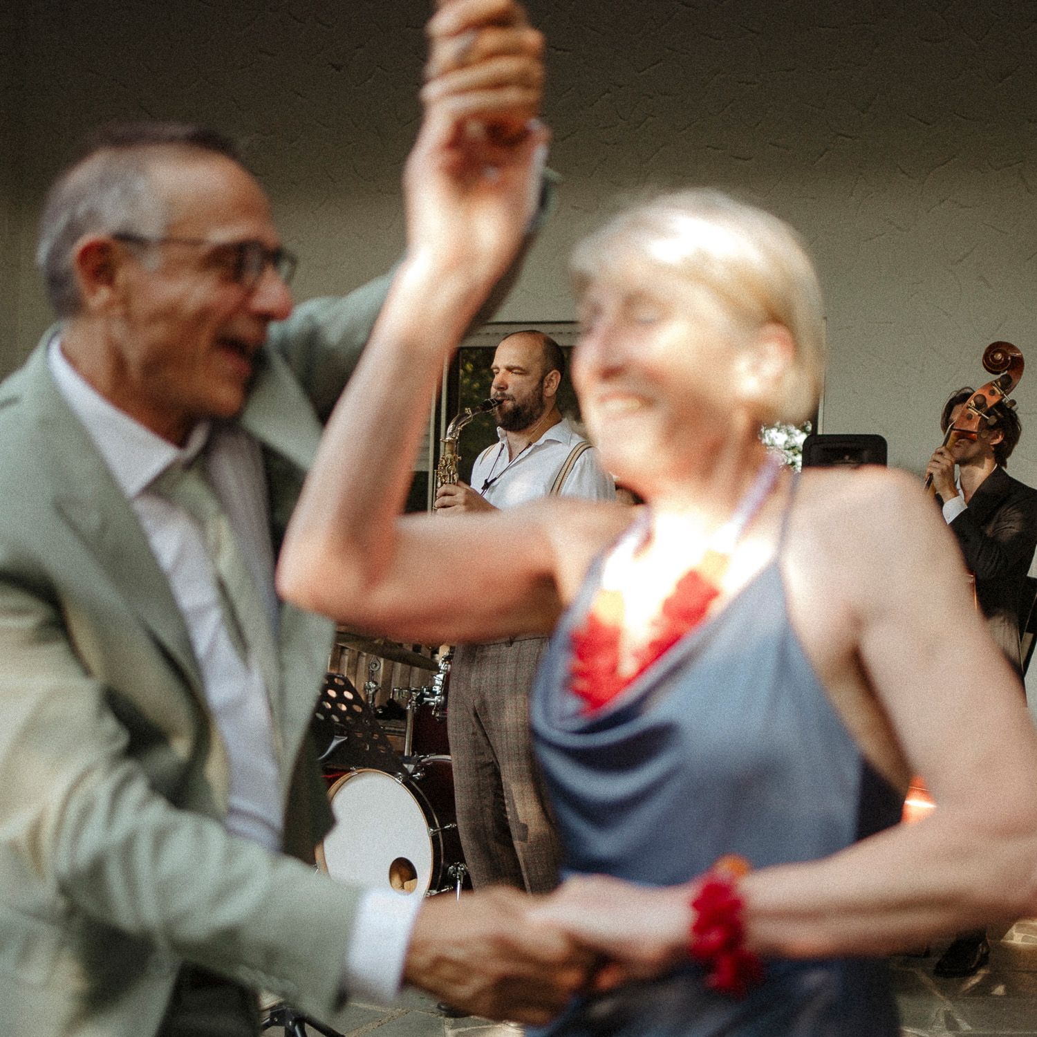 Couples dancing together at a social gathering with musicians performing in the background.