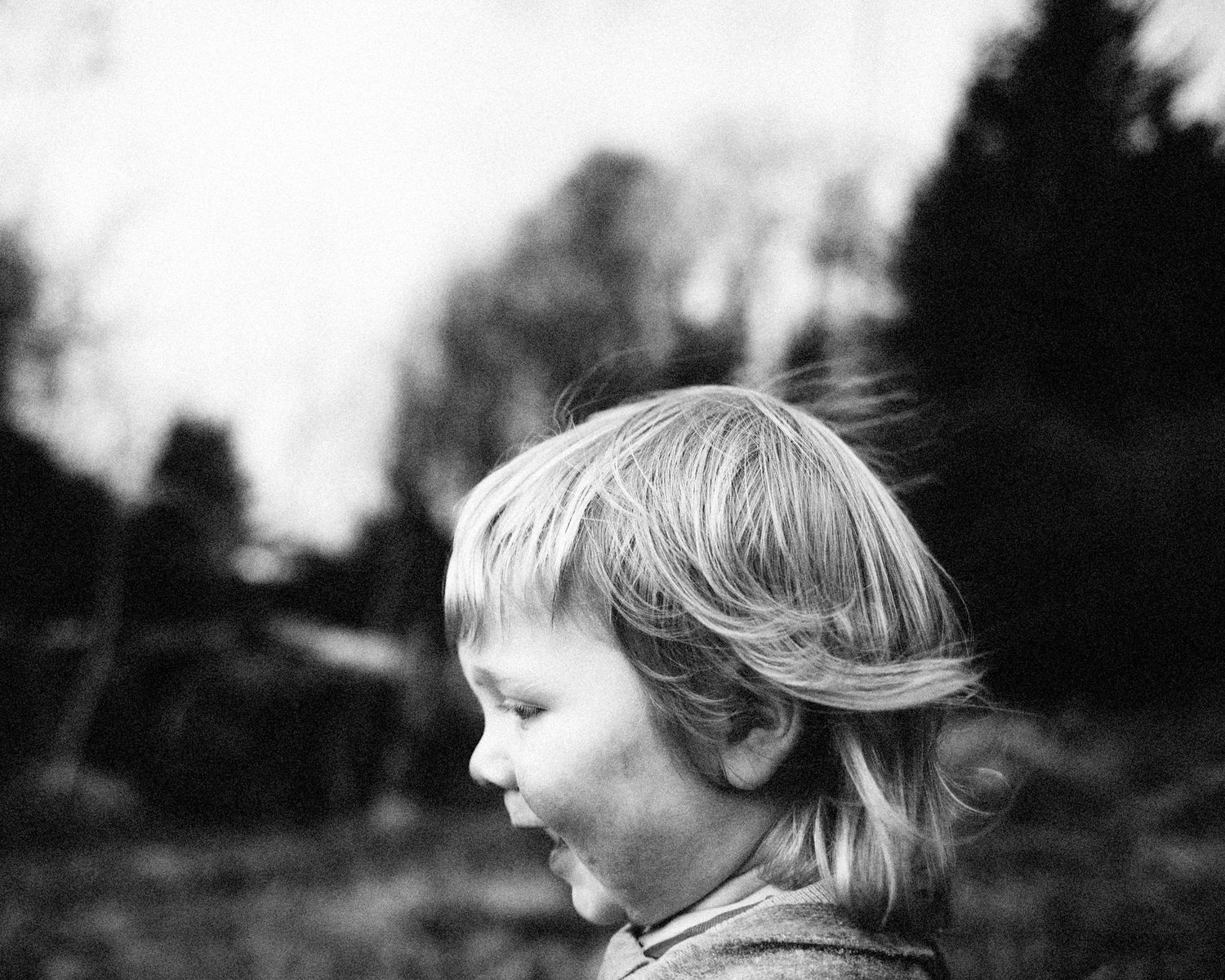 Black and white profile portrait showing windswept hair against a blurred background.