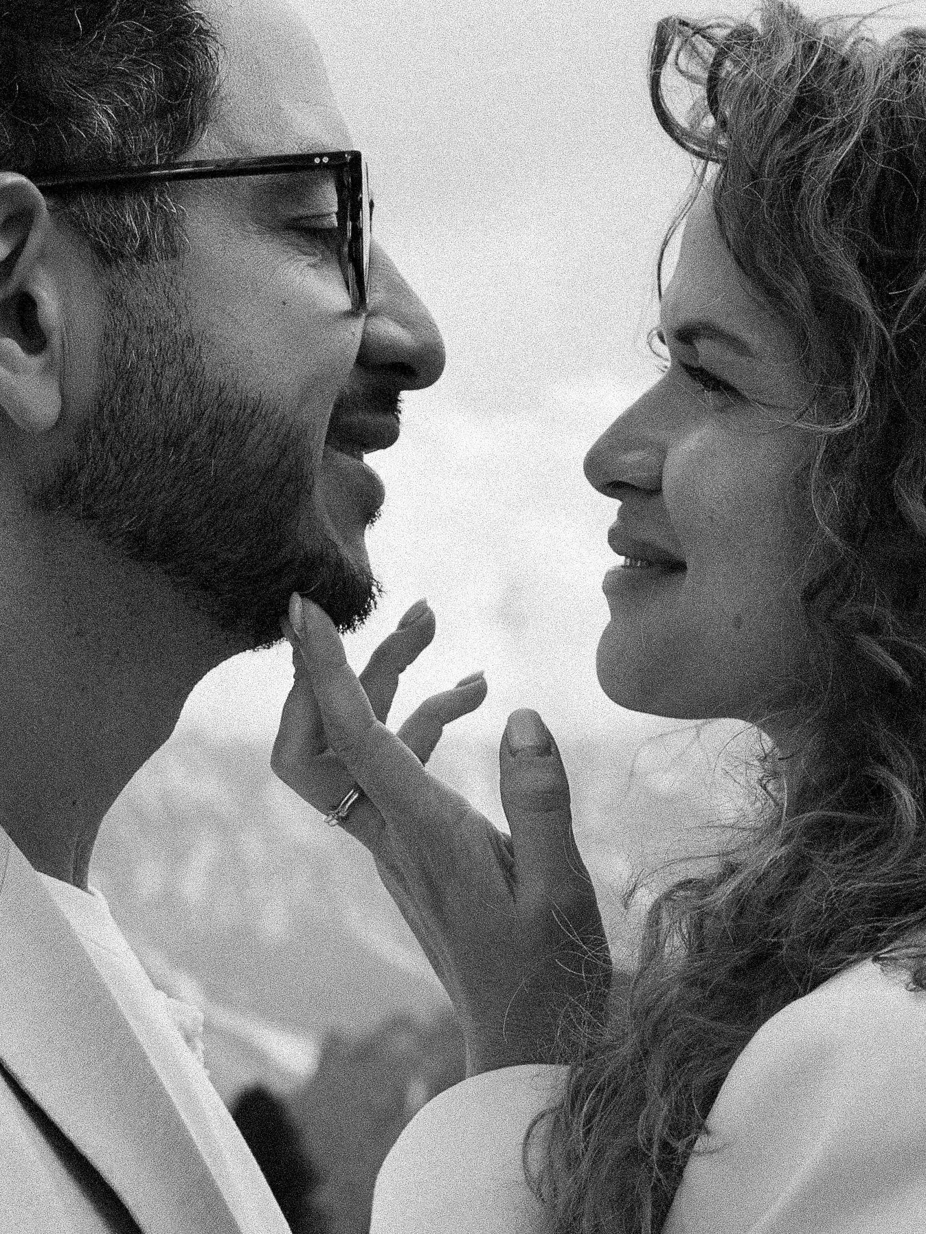 Black and white photo of a couple sharing a tender moment, woman touching man's face, both smiling softly.