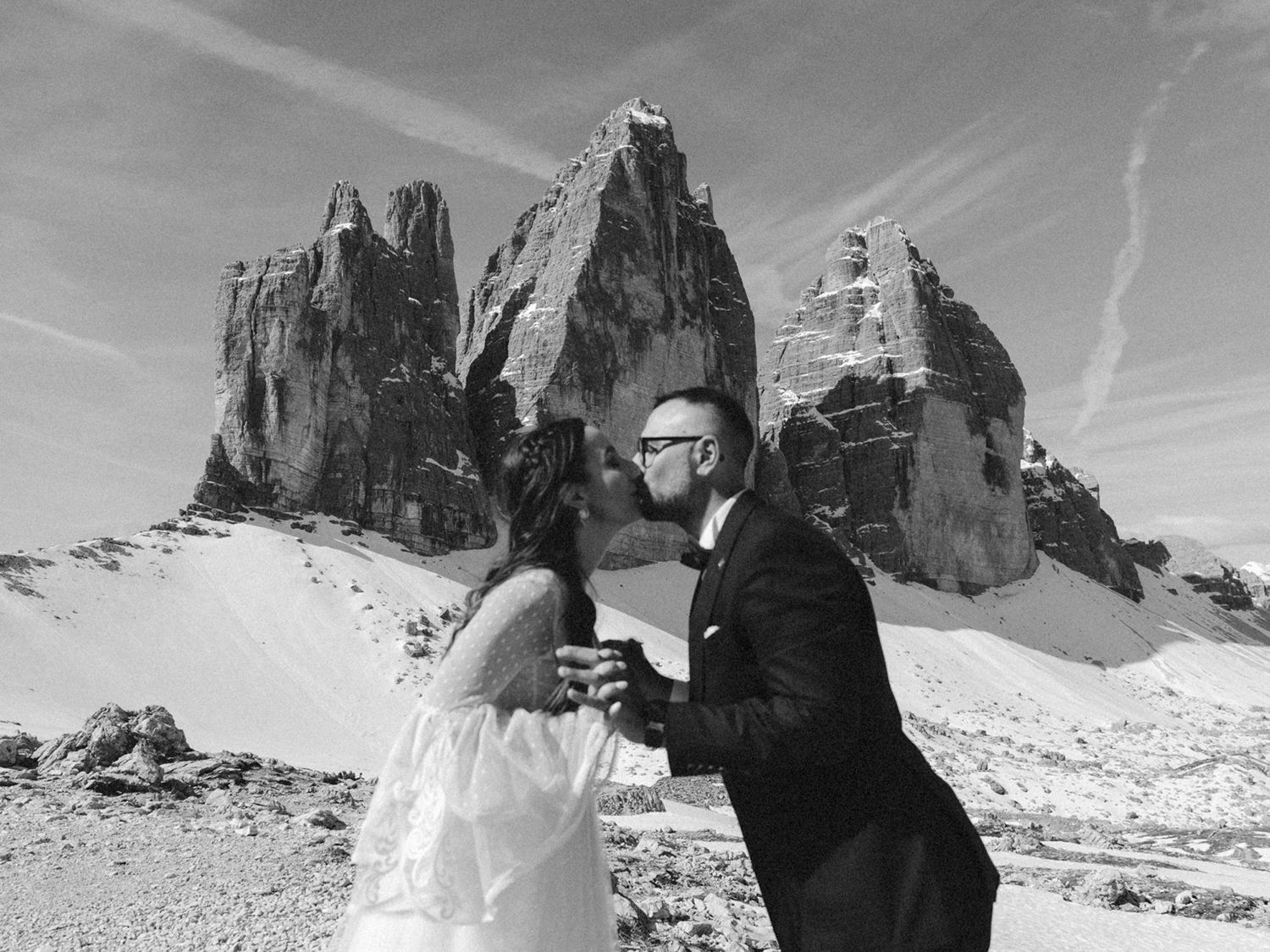 A black and white panoramic view of snow-covered mountain peaks against a bright sky with dramatic rock formations.