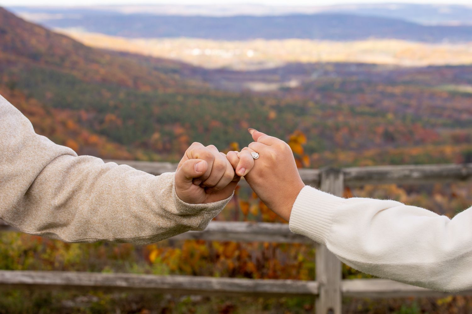 Two people making a pinky promise with autumn foliage and mountain valley scenic overlook in the background.