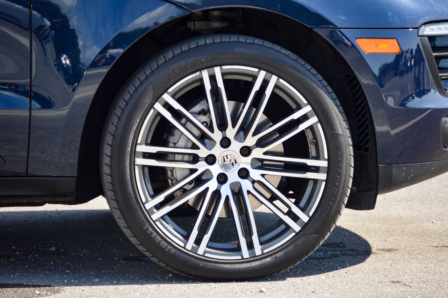Close-up of a dark blue car's alloy wheel with multi-spoke design and low-profile tire on pavement.