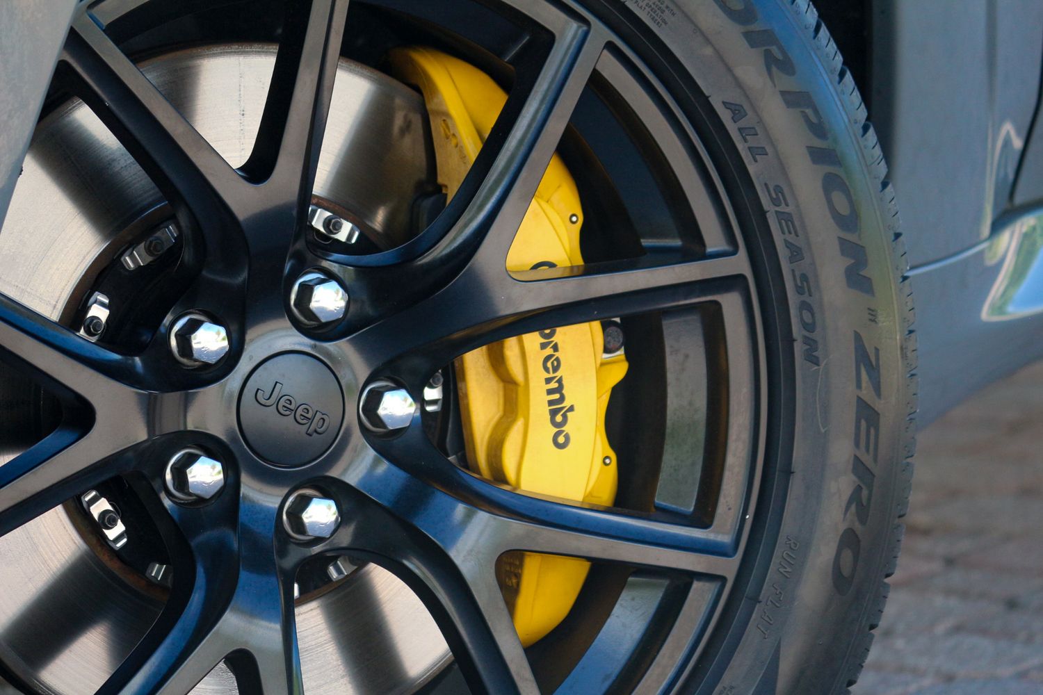 Close-up of a Jeep wheel featuring a yellow Brembo brake caliper and Pirelli P Zero tire on a dark alloy rim.
