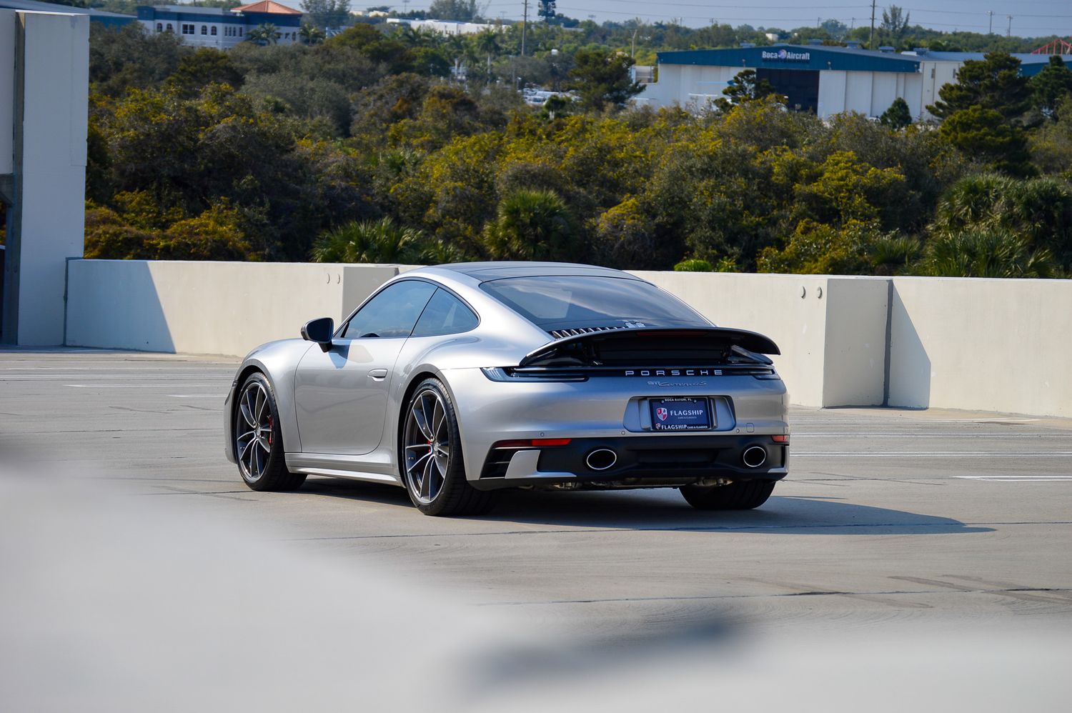 Silver Porsche 911 rear view on rooftop parking lot with city skyline and trees in background.
