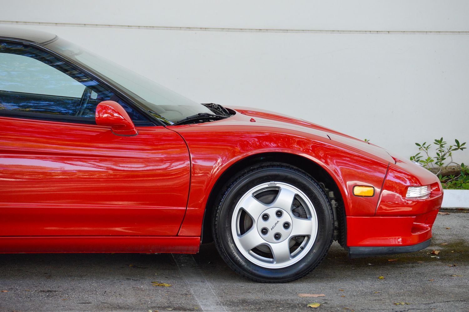 Red sports car with white alloy wheels parked on pavement, showcasing sleek aerodynamic body lines and targa top design.