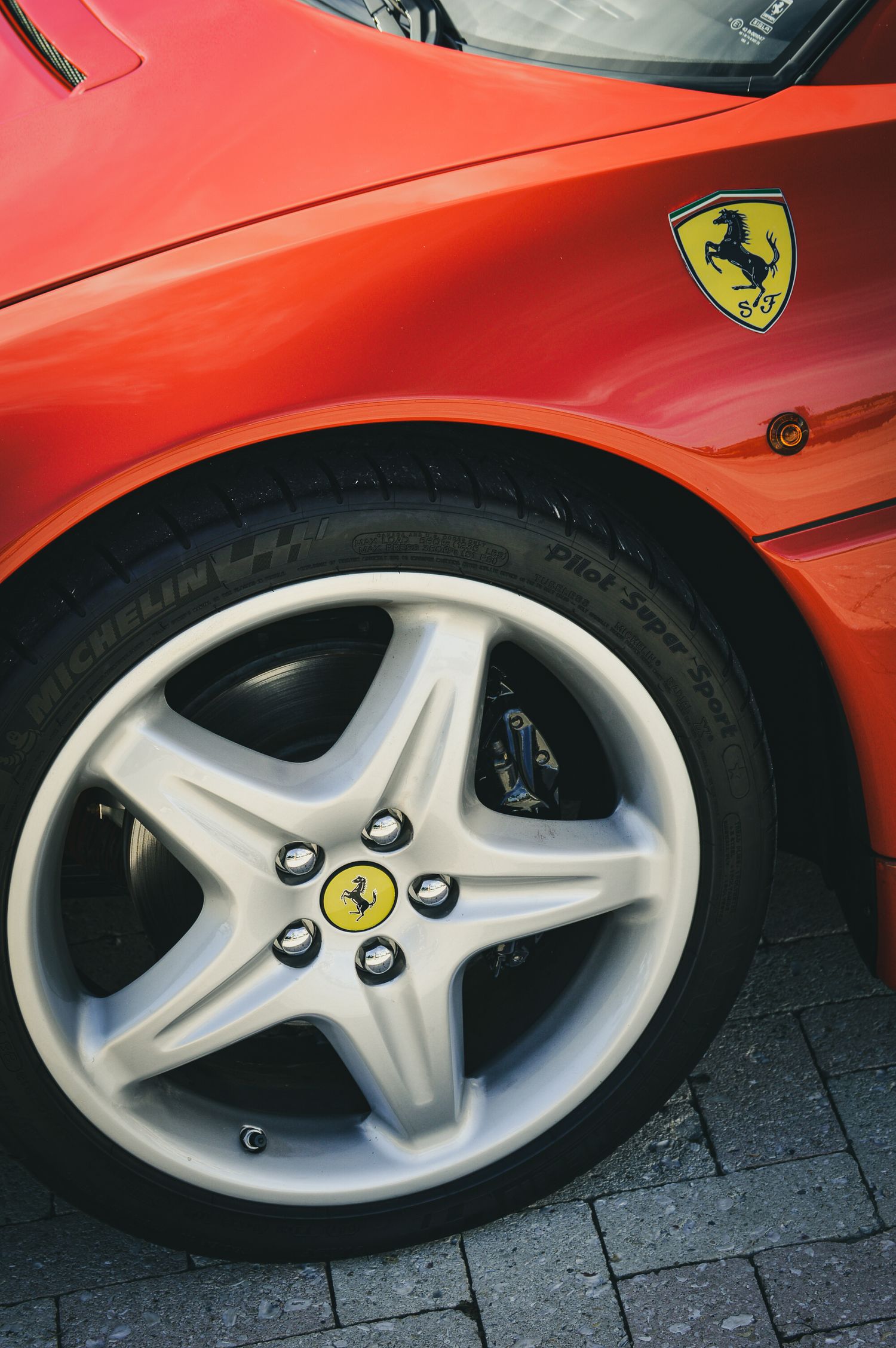 Close-up of a red Ferrari's Michelin tire and five-spoke alloy wheel with iconic prancing horse logo on the hub.