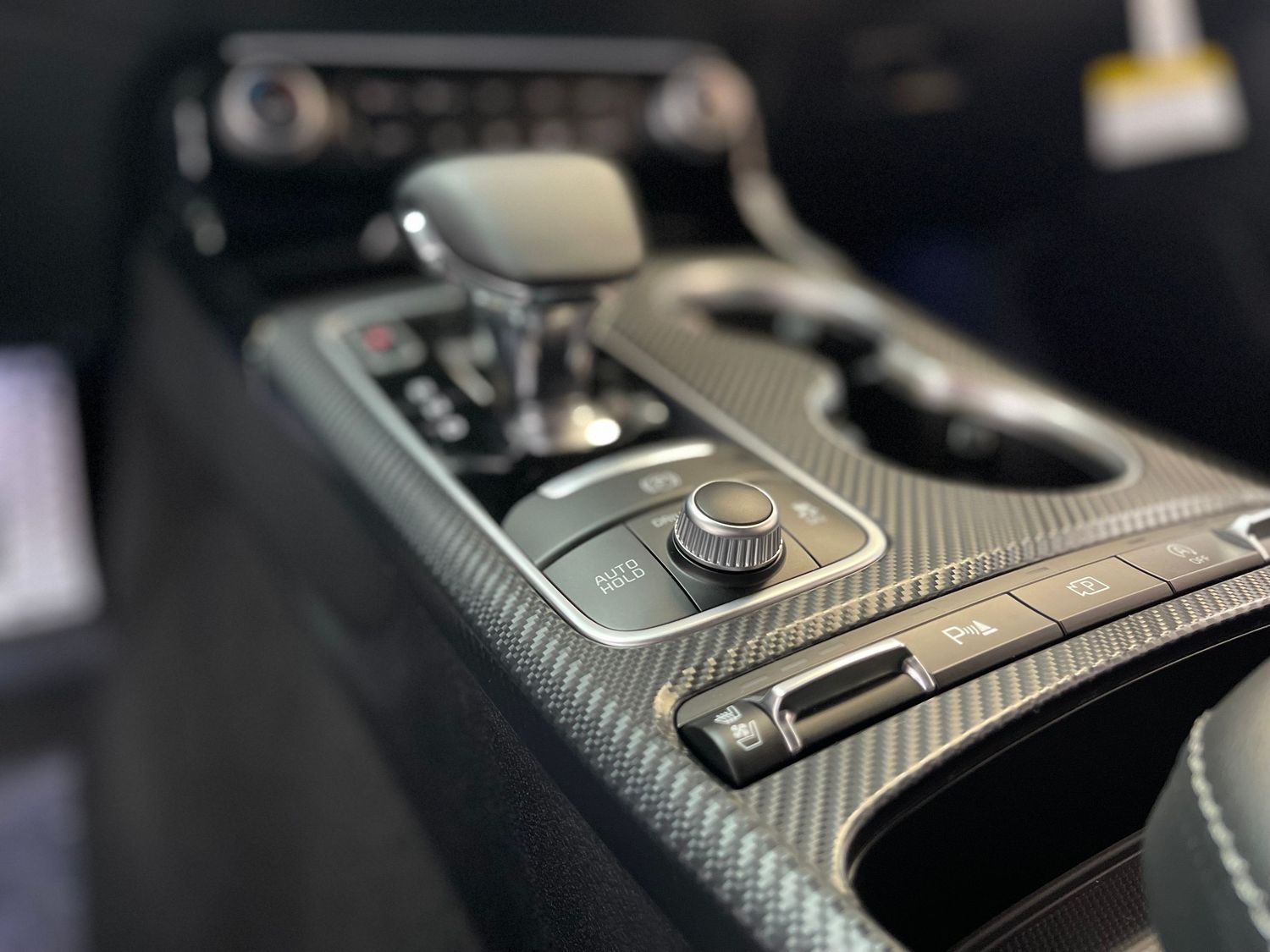 Close-up of modern car interior showing gear shifter and carbon fiber trim.