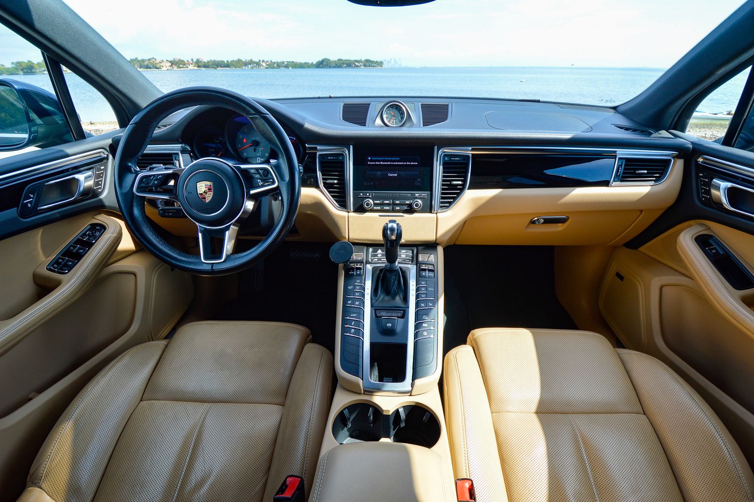 Luxurious tan leather interior of a Porsche Macan SUV with carbon fiber trim and modern infotainment system.