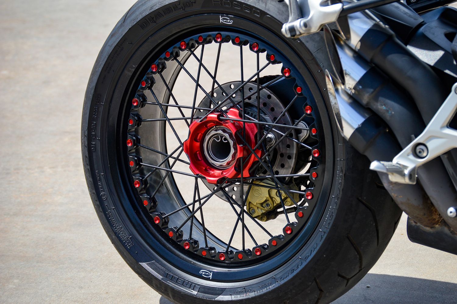 Close-up of a motorcycle wheel with red hub, black spokes, and red accent bolts on a sleek black tire.