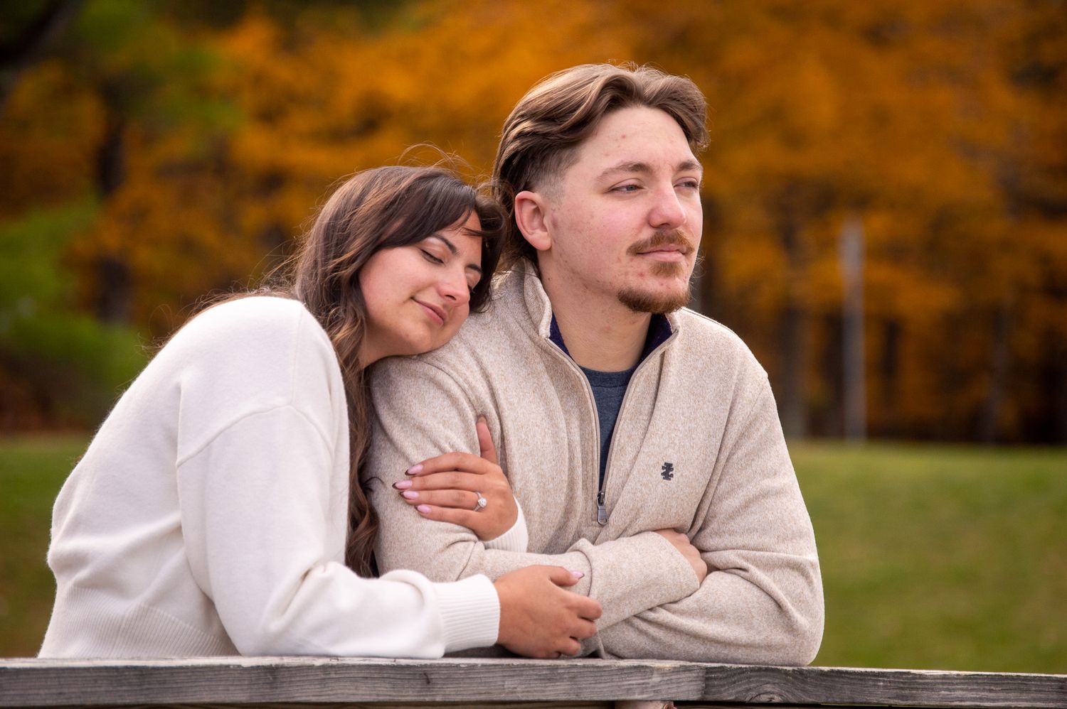 Couple embracing on a bench with vibrant autumn foliage in the background during a fall outdoor photoshoot.