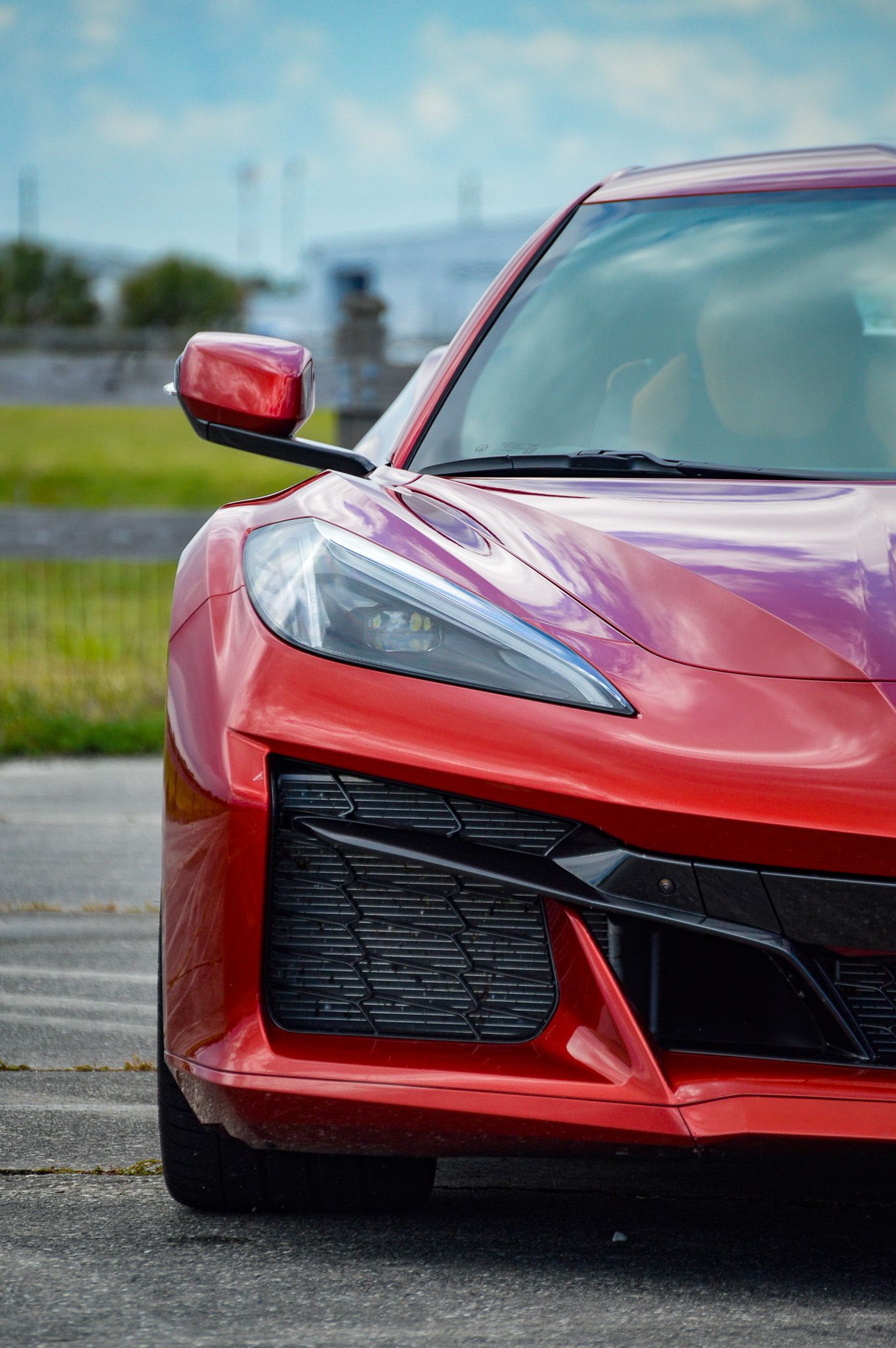 Red Chevrolet Corvette C8 sports car front quarter view on track, showcasing aggressive styling and LED headlights.