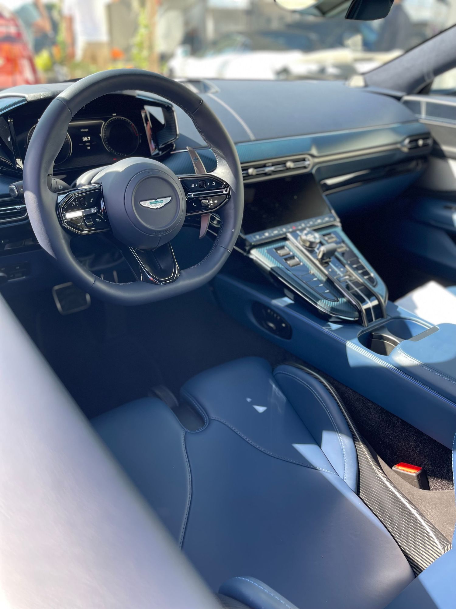 Sleek modern interior of an Aston Martin luxury car showing the steering wheel and dashboard with blue leather accents.
