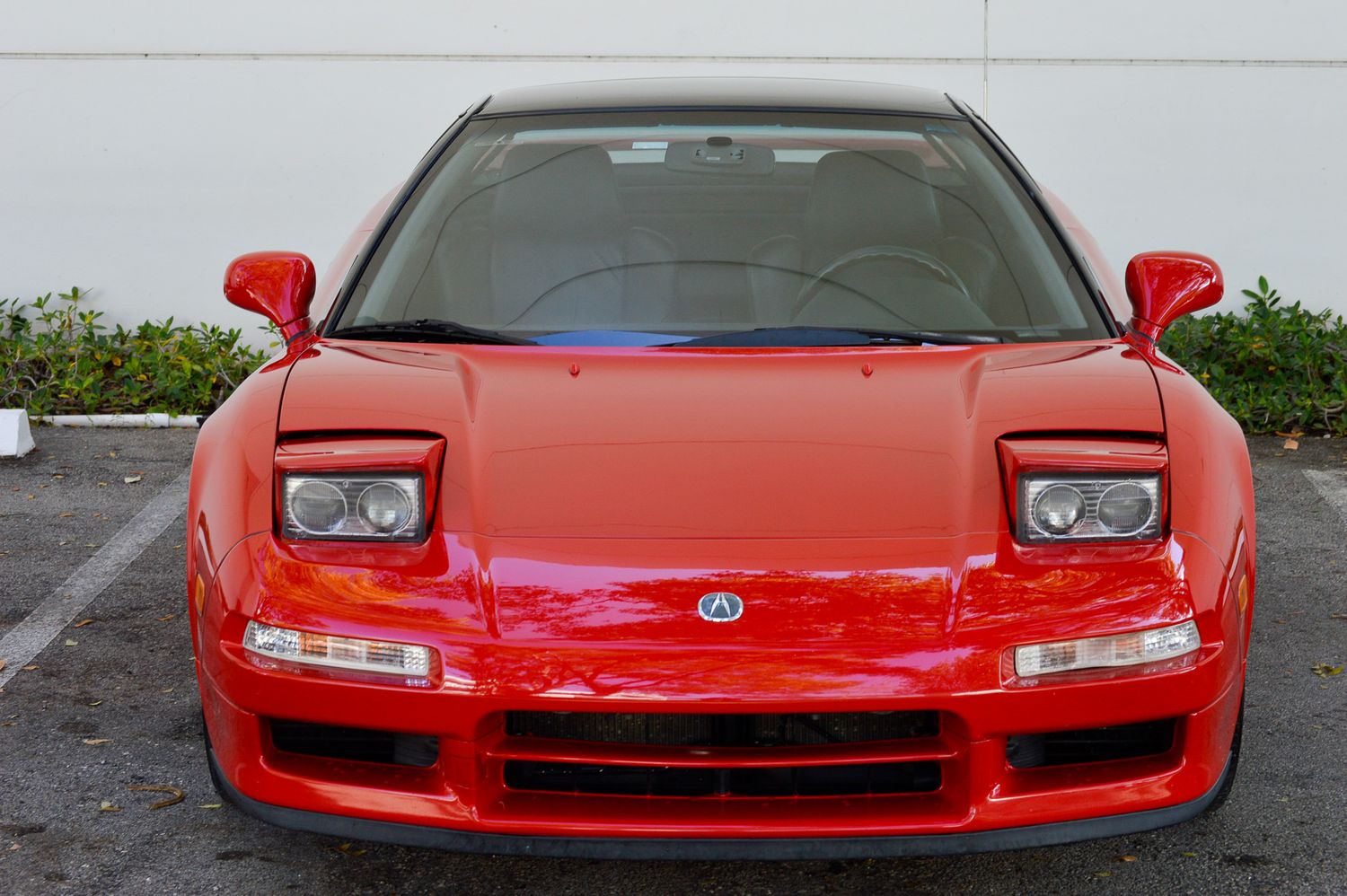 Red Acura NSX sports car front view in parking lot, showcasing sleek aerodynamic design and pop-up headlights.