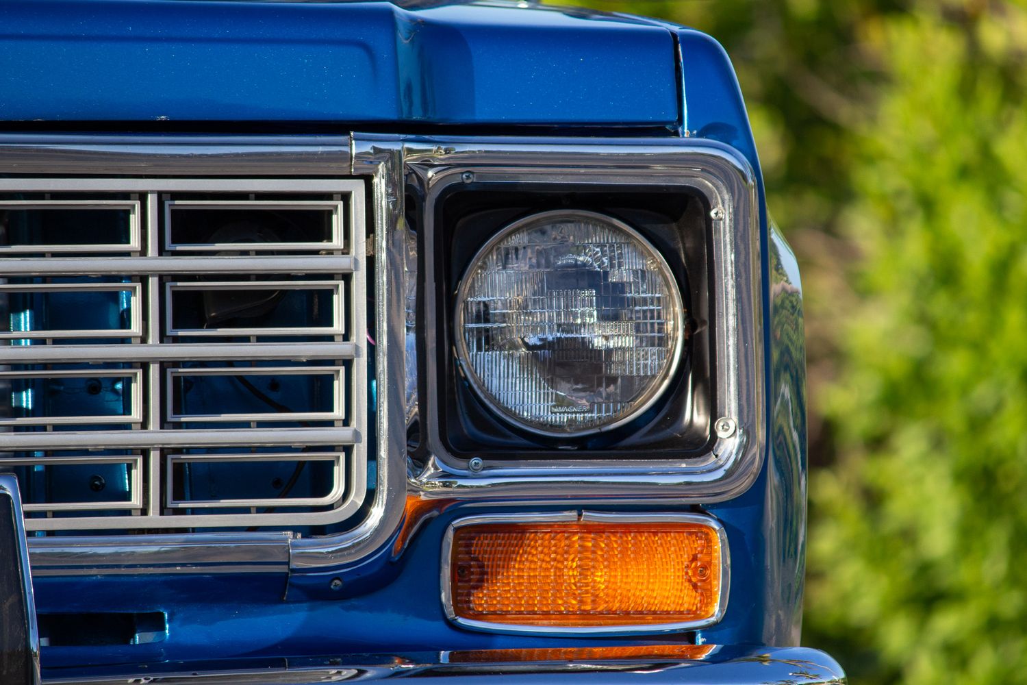 Close-up of a classic blue truck headlight and chrome grille, showcasing vintage American automotive design.