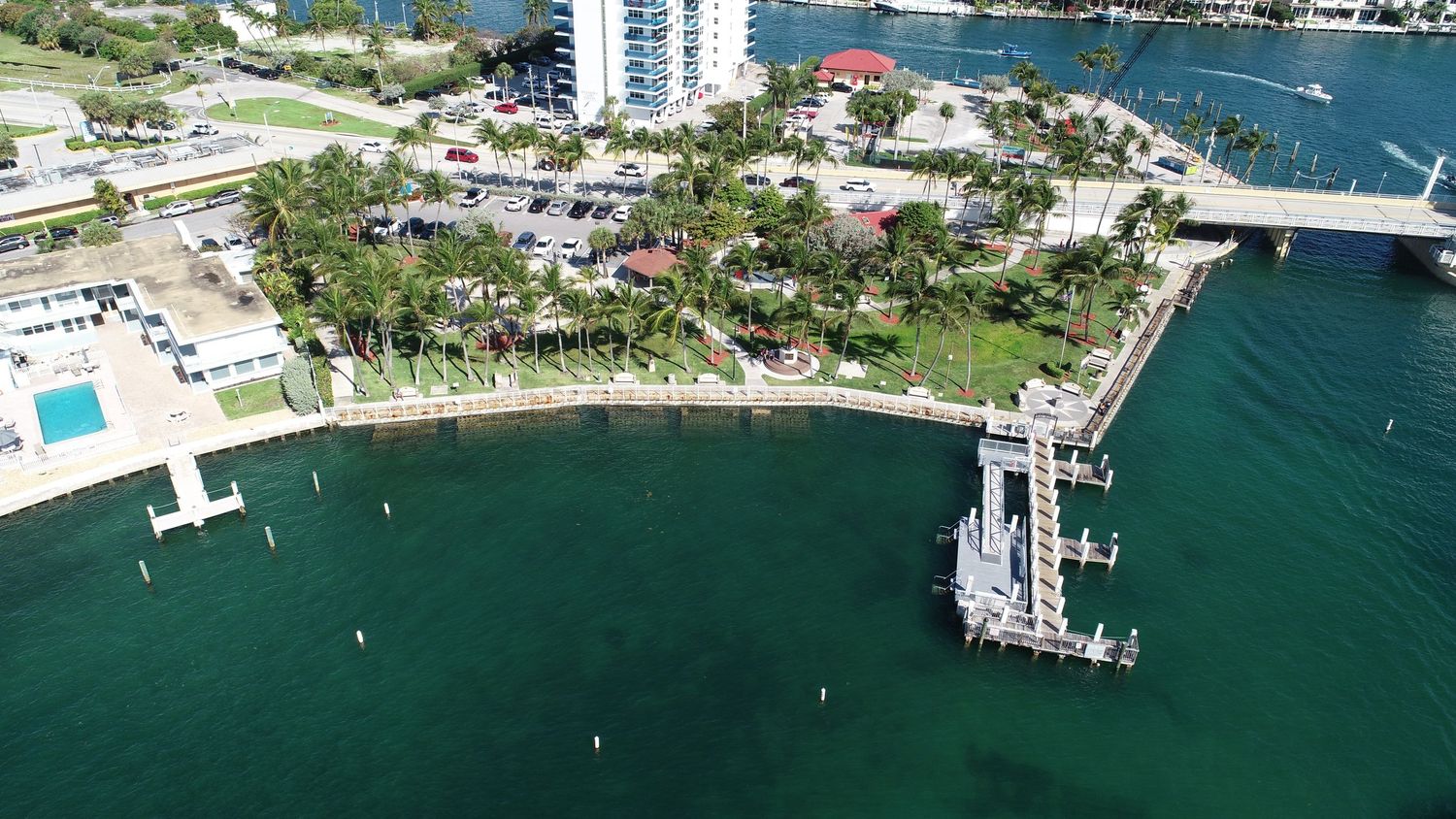 Aerial view of a coastal Florida waterfront park with a pier, palm trees, and turquoise water.