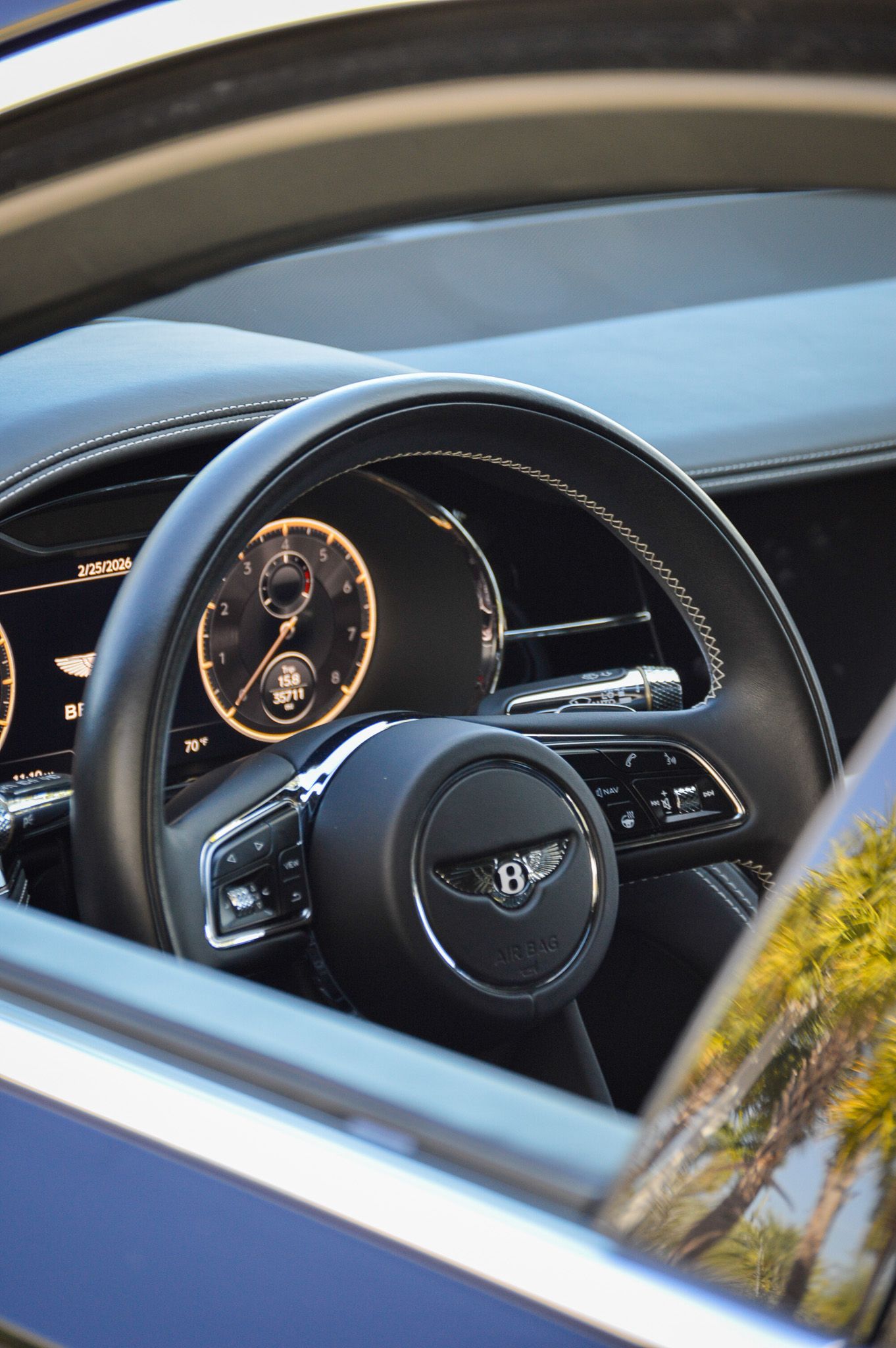 Bentley luxury car interior featuring a leather steering wheel with emblem, illuminated dashboard gauges, and premium controls.