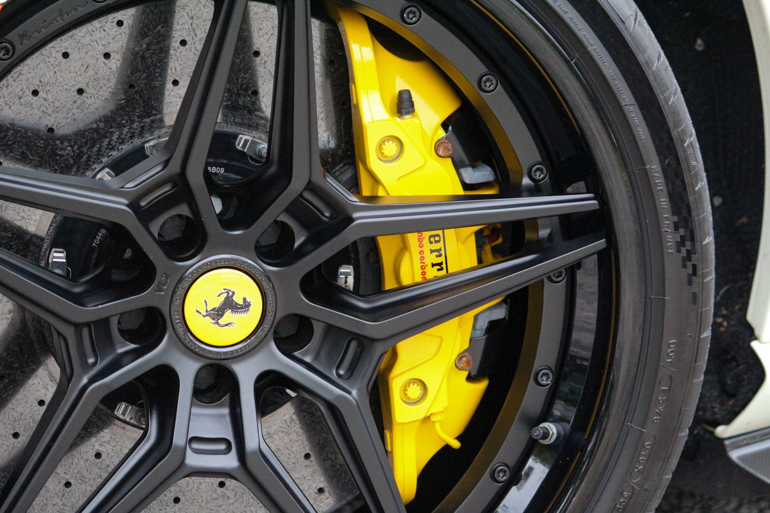 Close-up of a Ferrari wheel with yellow brake calipers and a prancing horse center cap on a dark alloy rim.