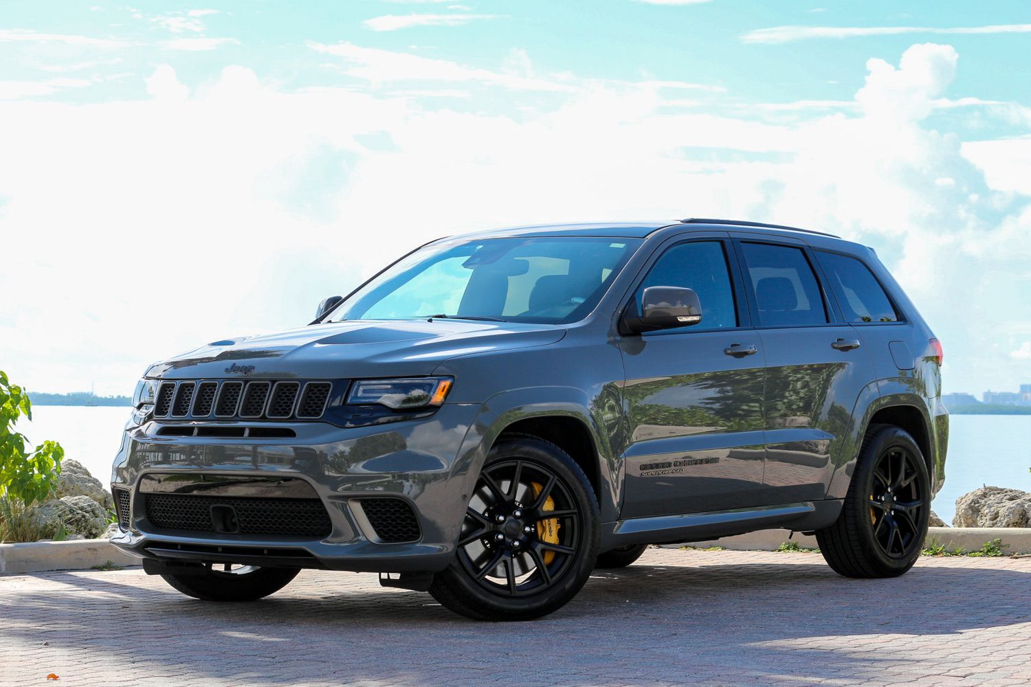Gray Jeep Grand Cherokee Trackhawk SUV parked near waterfront on a sunny day with black wheels and aggressive stance.