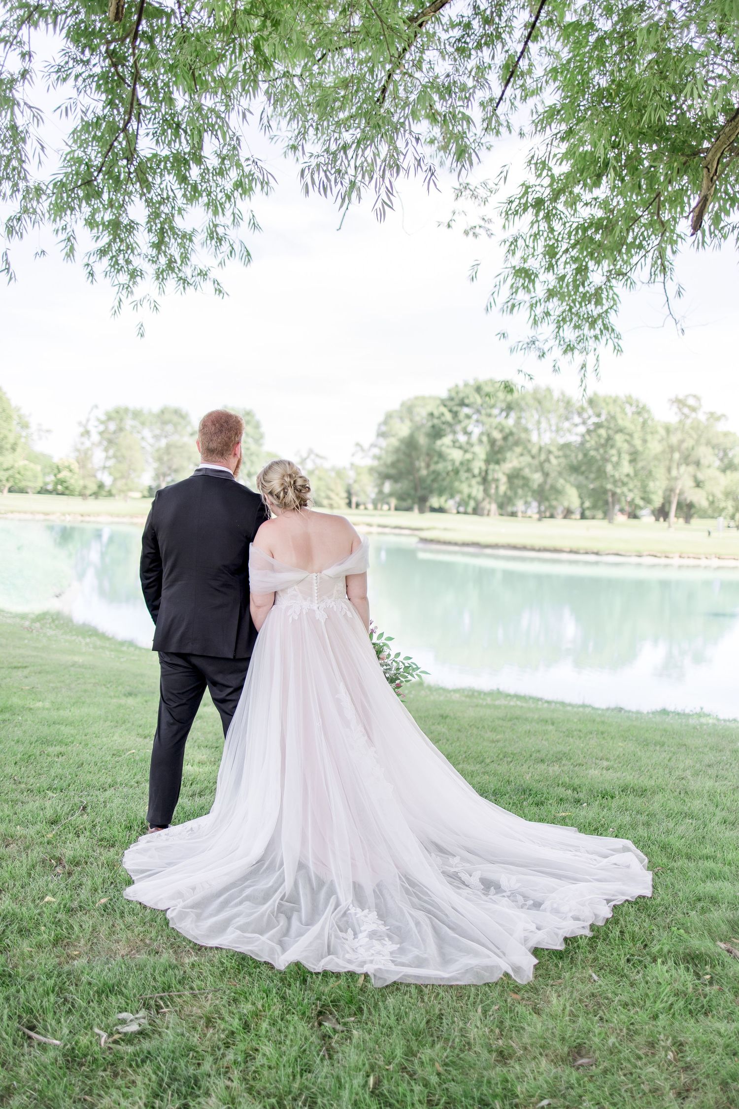 Elegant wedding couple posing by lakeside with flowing white dress and veil.
