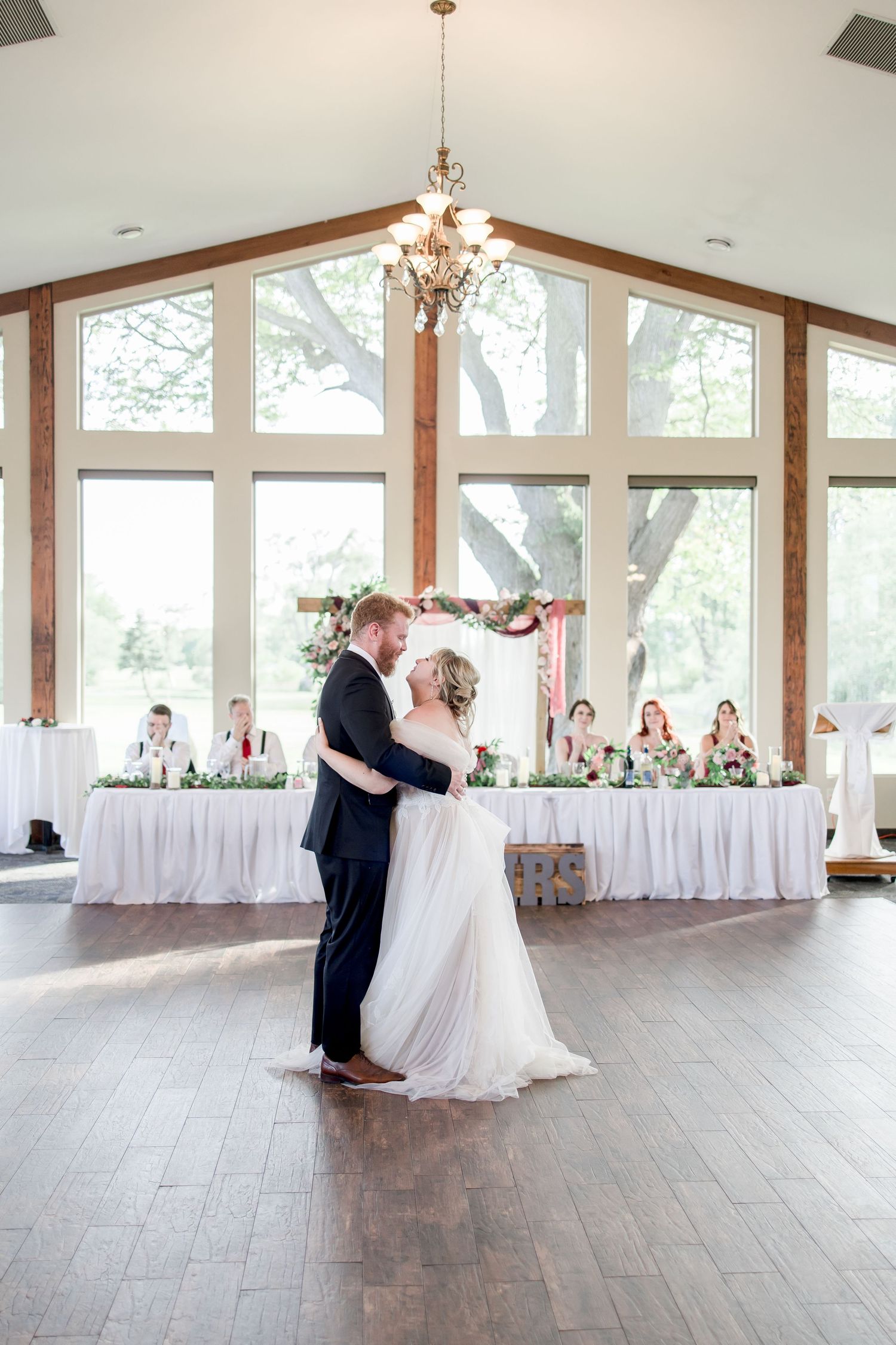 Couple dancing together in elegant reception venue with hardwood floors and natural lighting.