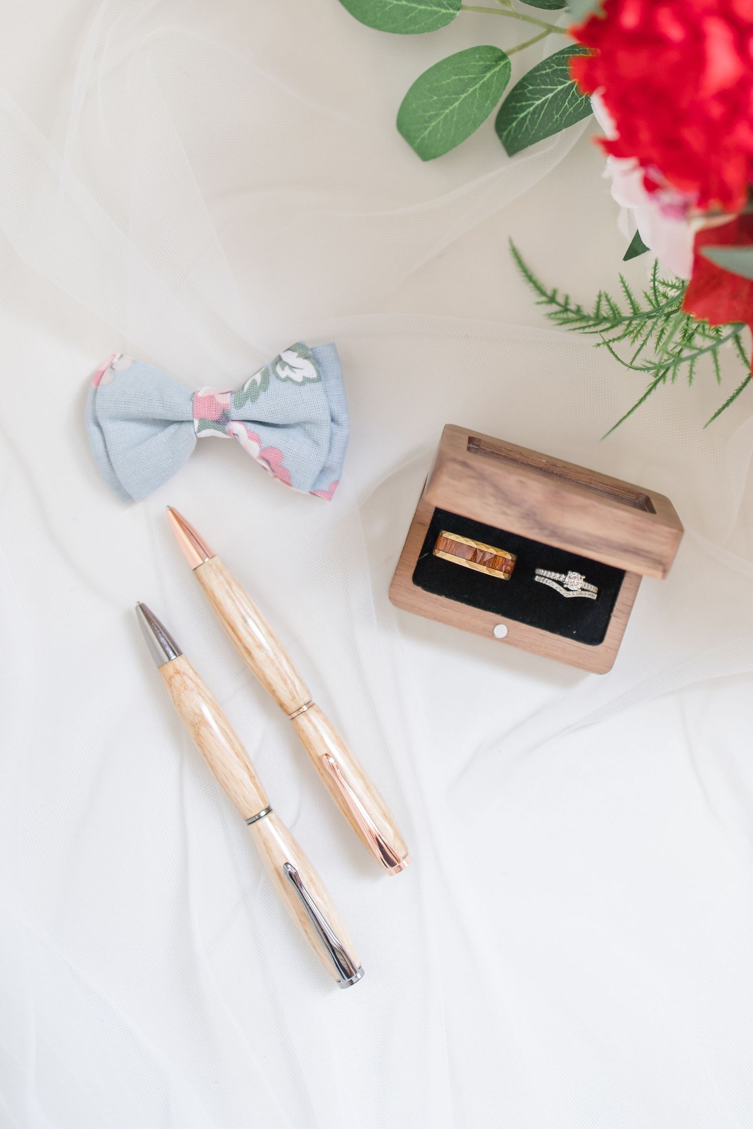 Rose gold pens and writing instruments arranged with red flowers on white background.