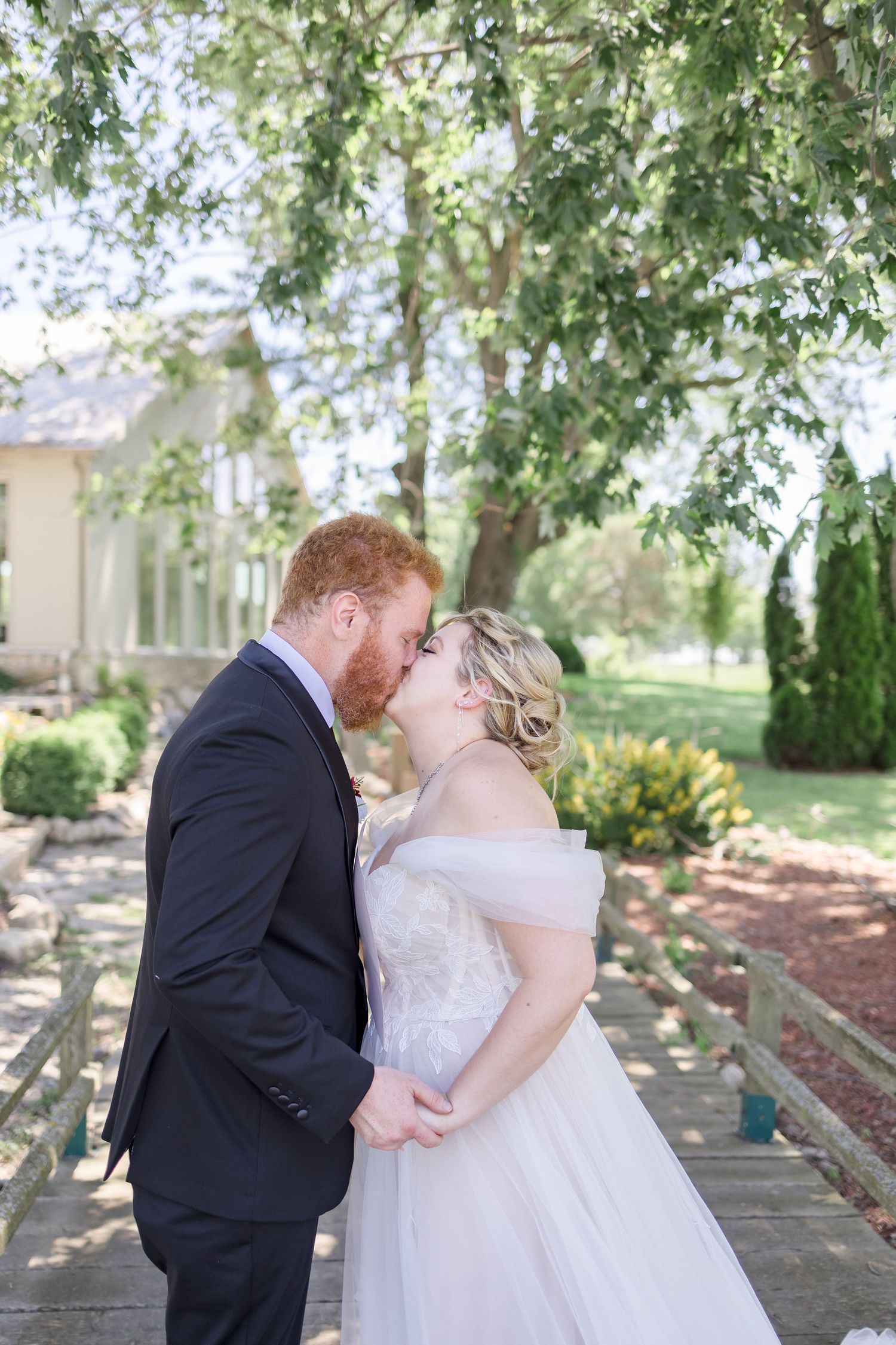 Romantic wedding couple sharing intimate moment under trees at outdoor venue.