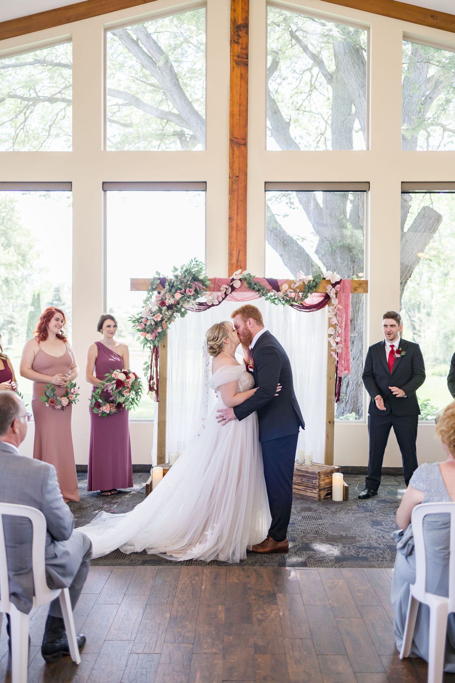 Wedding ceremony setup in rustic indoor venue with floral arch and white chairs.