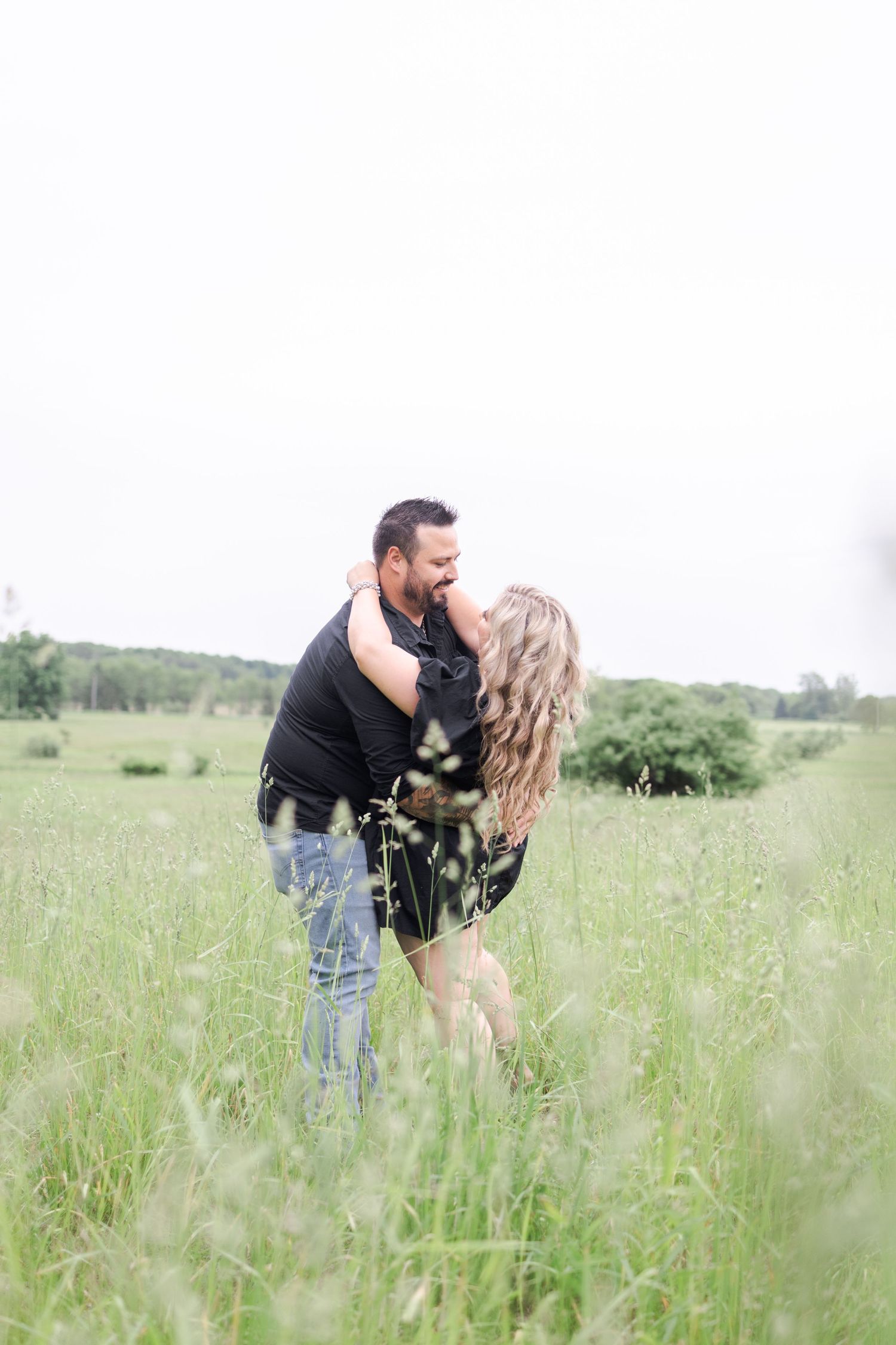 Romantic couple sharing intimate moments in a sunlit meadow with tall grass.