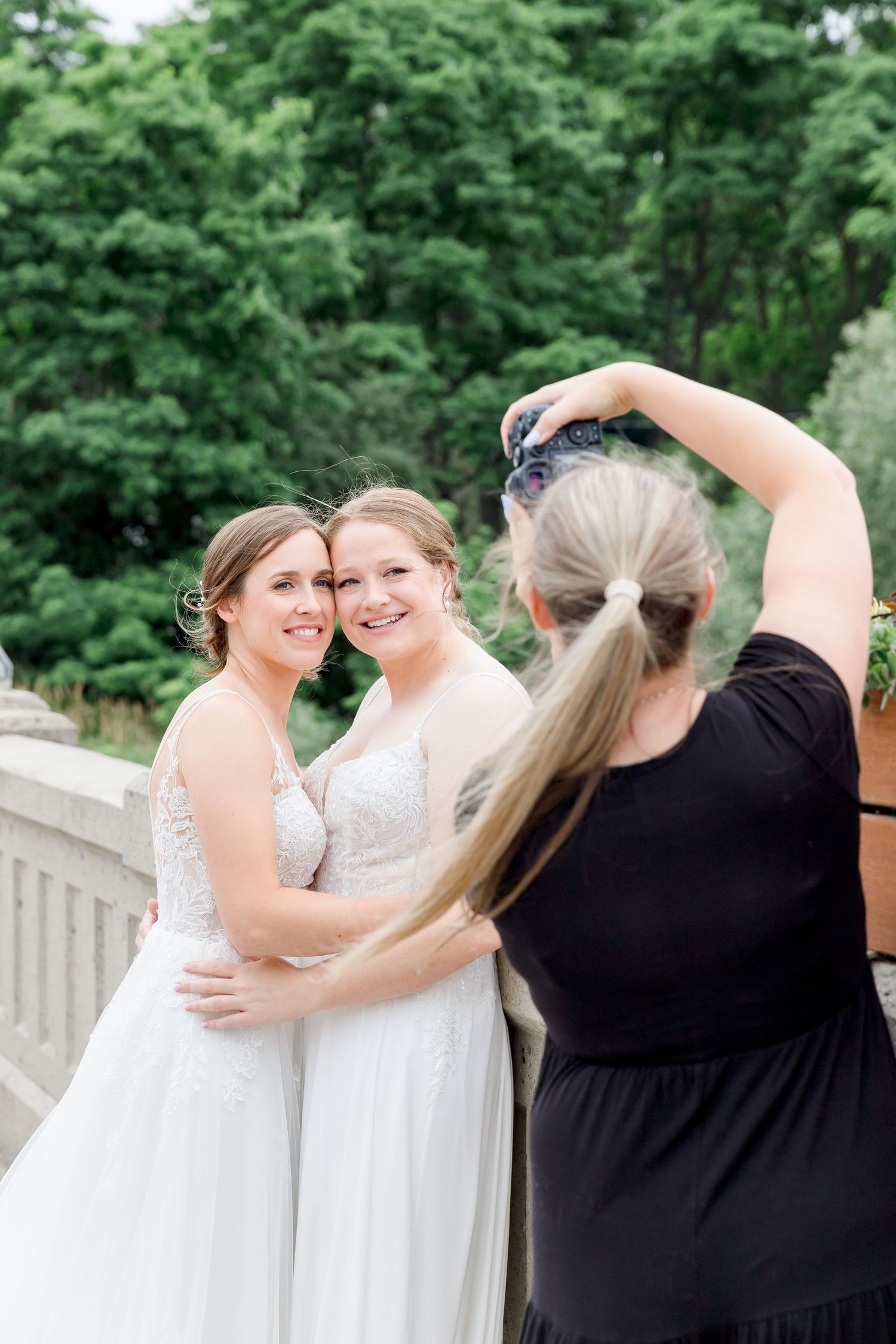 Wedding party members share candid laughs and embraces on a sunny outdoor deck.