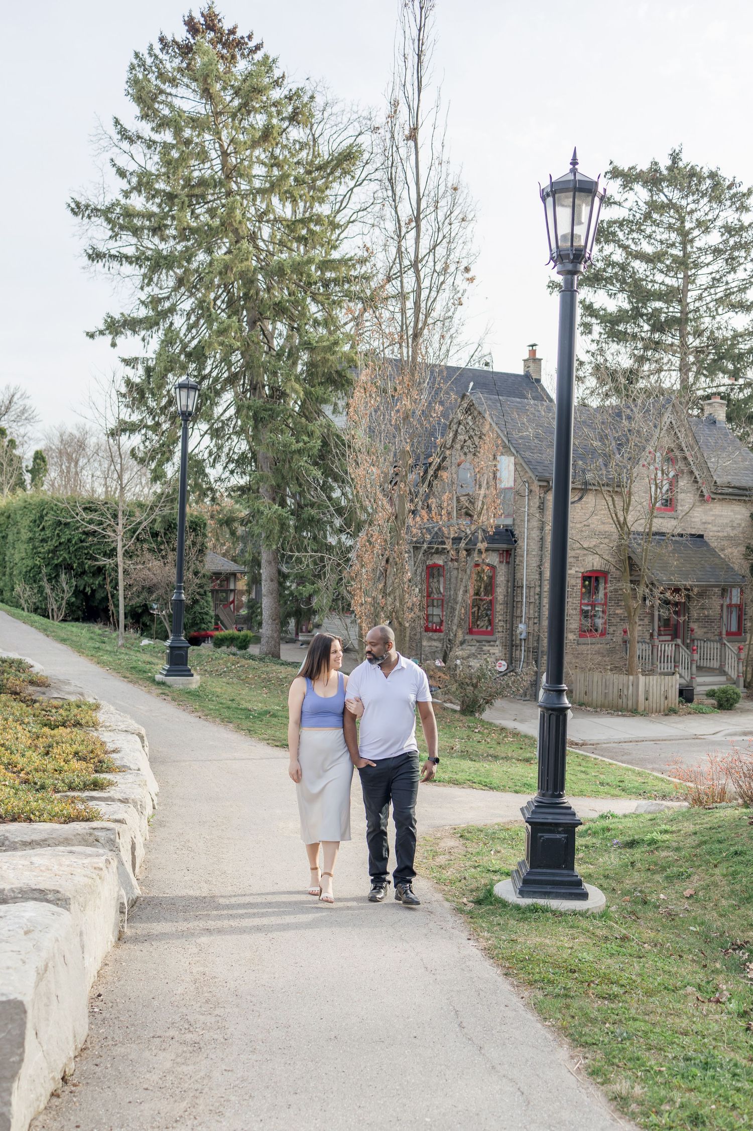 Couple strolling along a winding pathway with historic buildings in the background.