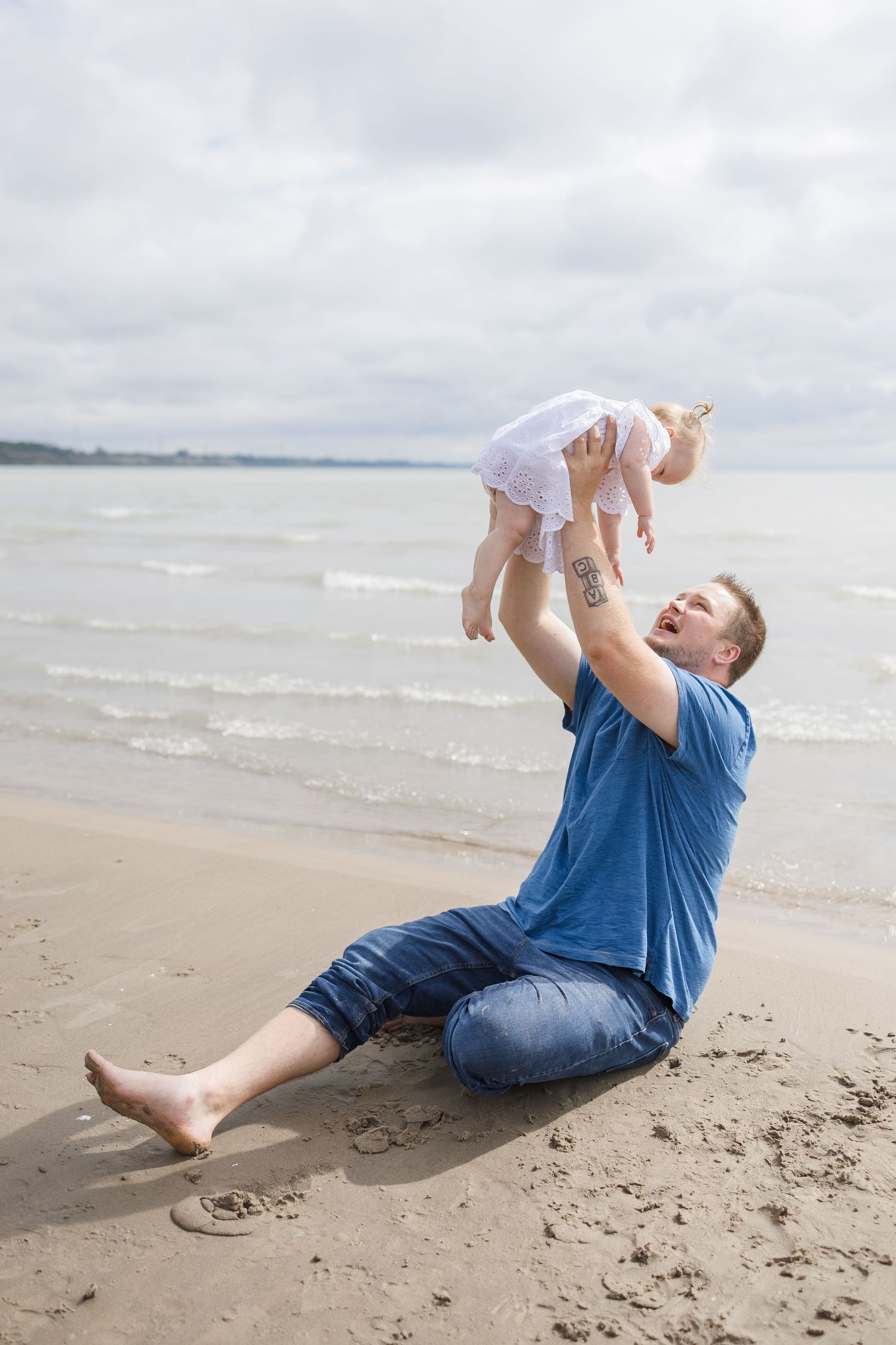 Parent lifting child in the air while playing on a beach.
