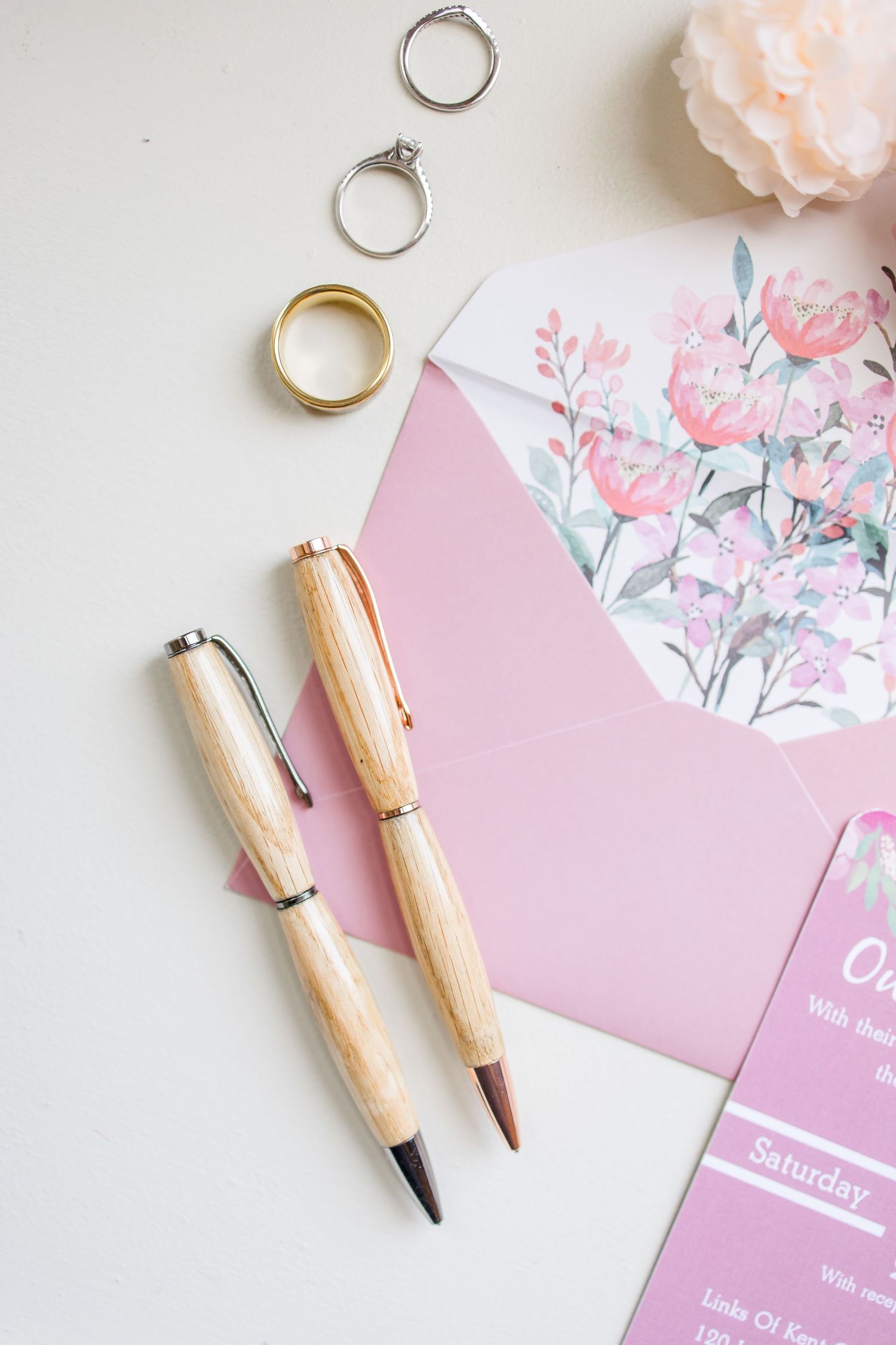 Pink stationery items and wooden pens arranged on a light surface with floral designs.
